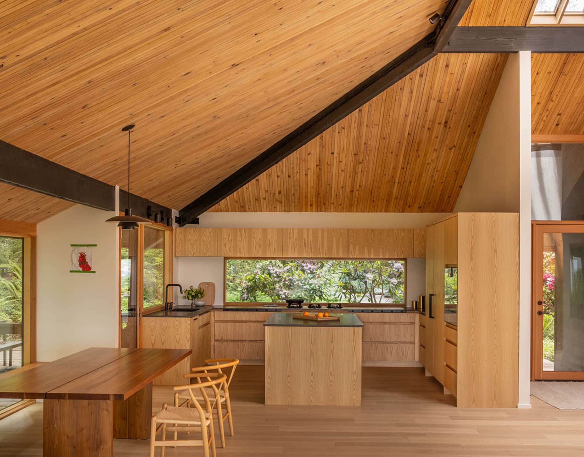 Contemporary residential kitchen featuring wooden cabinets, open floor plan, and large windows.