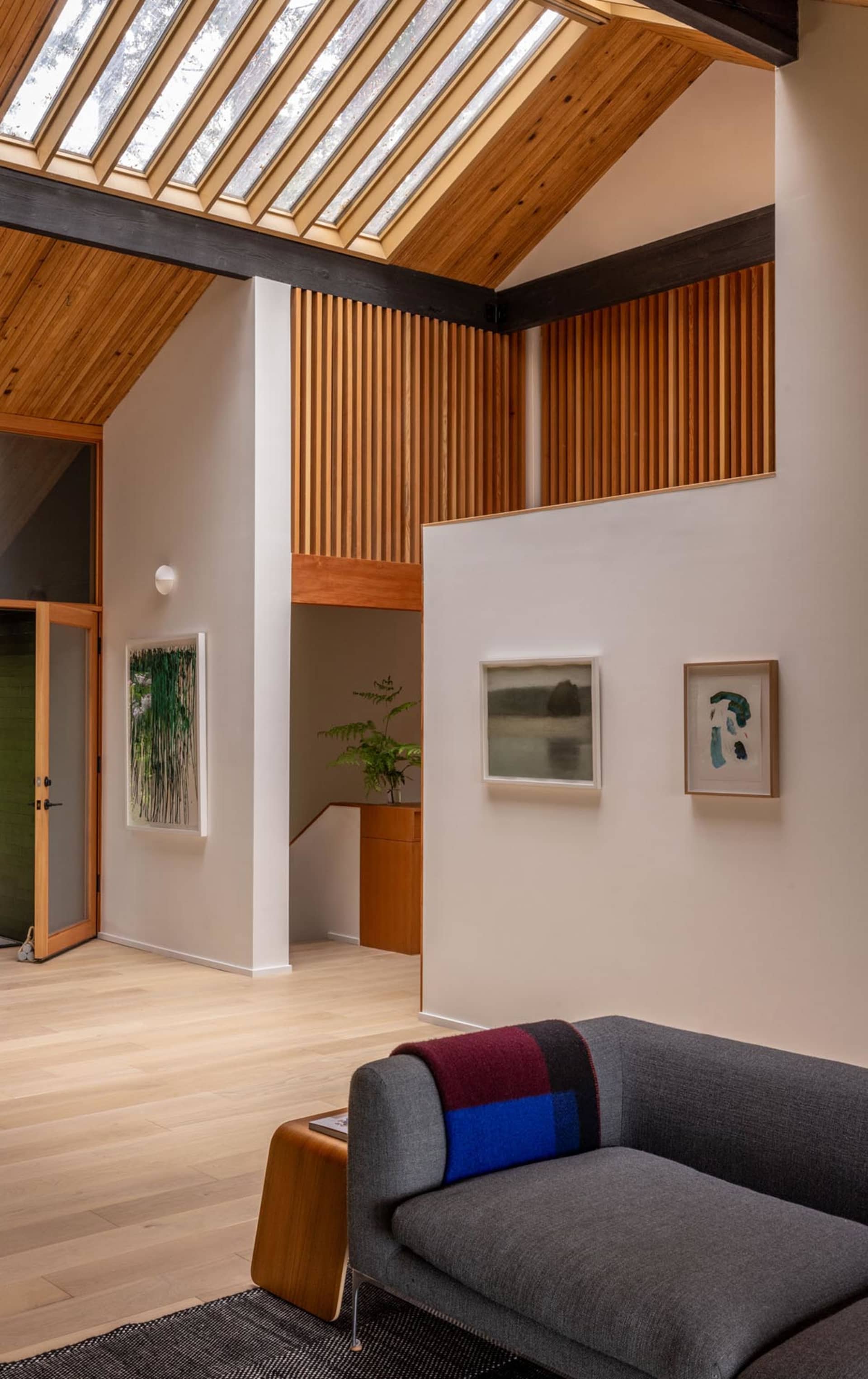 A contemporary living room featuring a wood-paneled wall and a gray sofa with a colorful throw blanket, under a slanted ceili