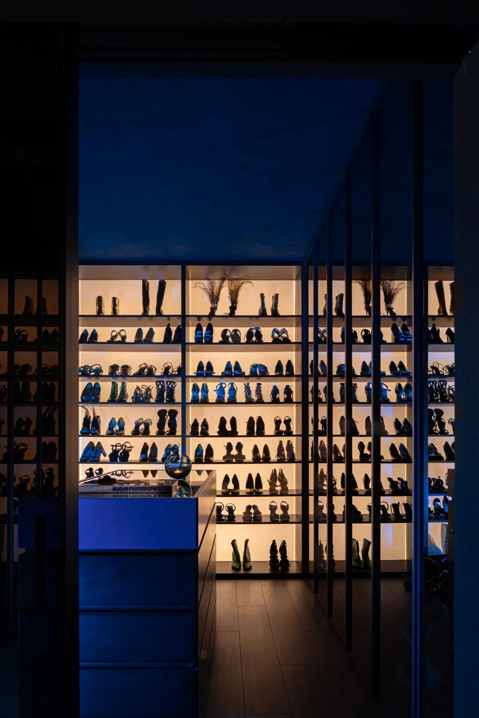 A glass-walled shoe closet filled with various high-heeled shoes.