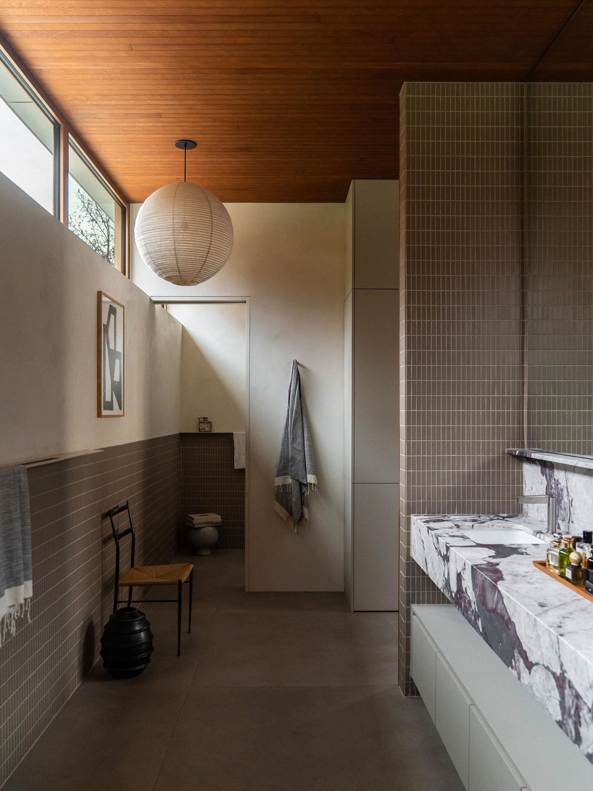 A modern bathroom featuring a marble sink counter and tiled walls with a paper lantern hanging from the ceiling.