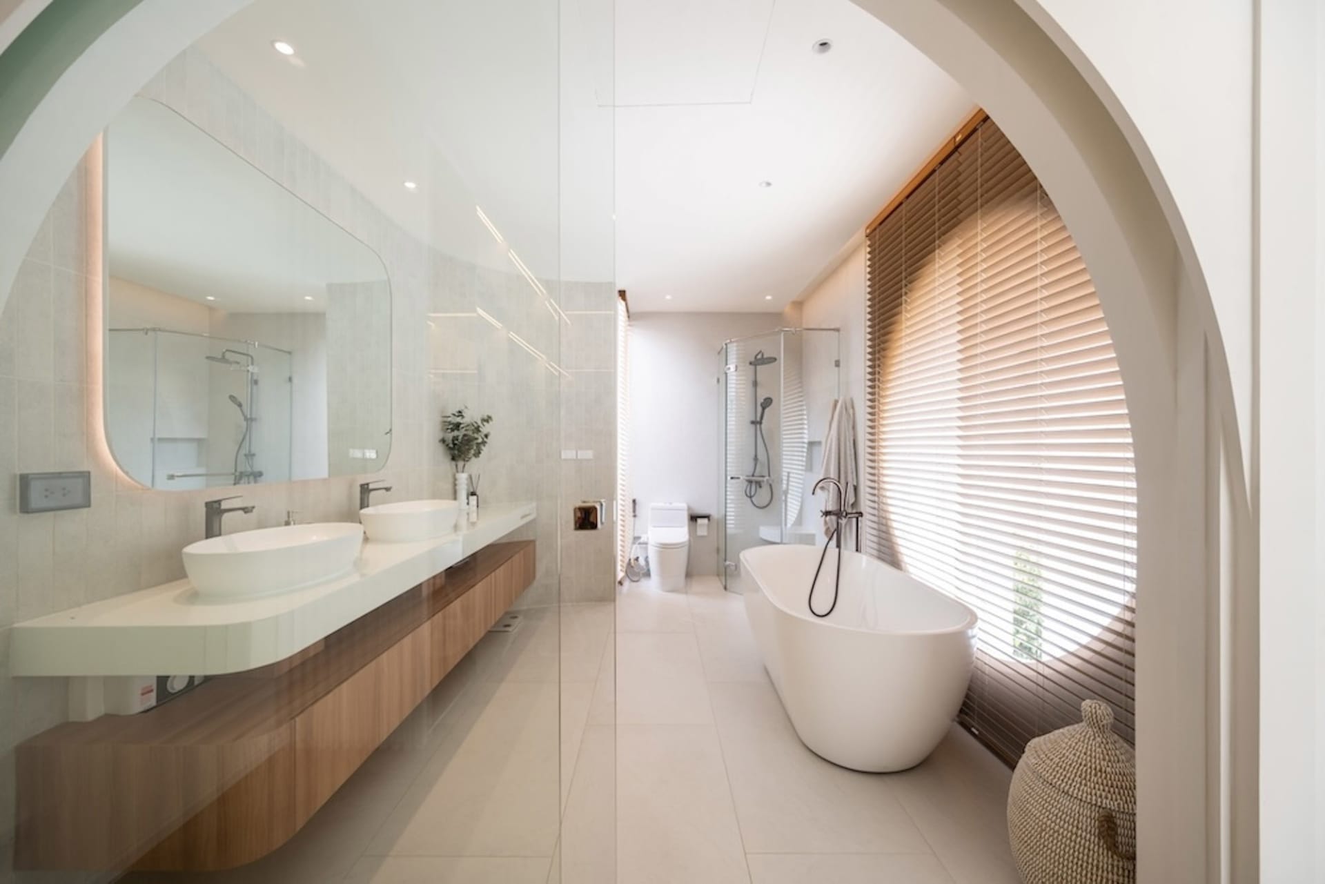Modern bathroom with tile, concrete, and wooden elements, featuring a freestanding tub, double sink vanity, and large window.