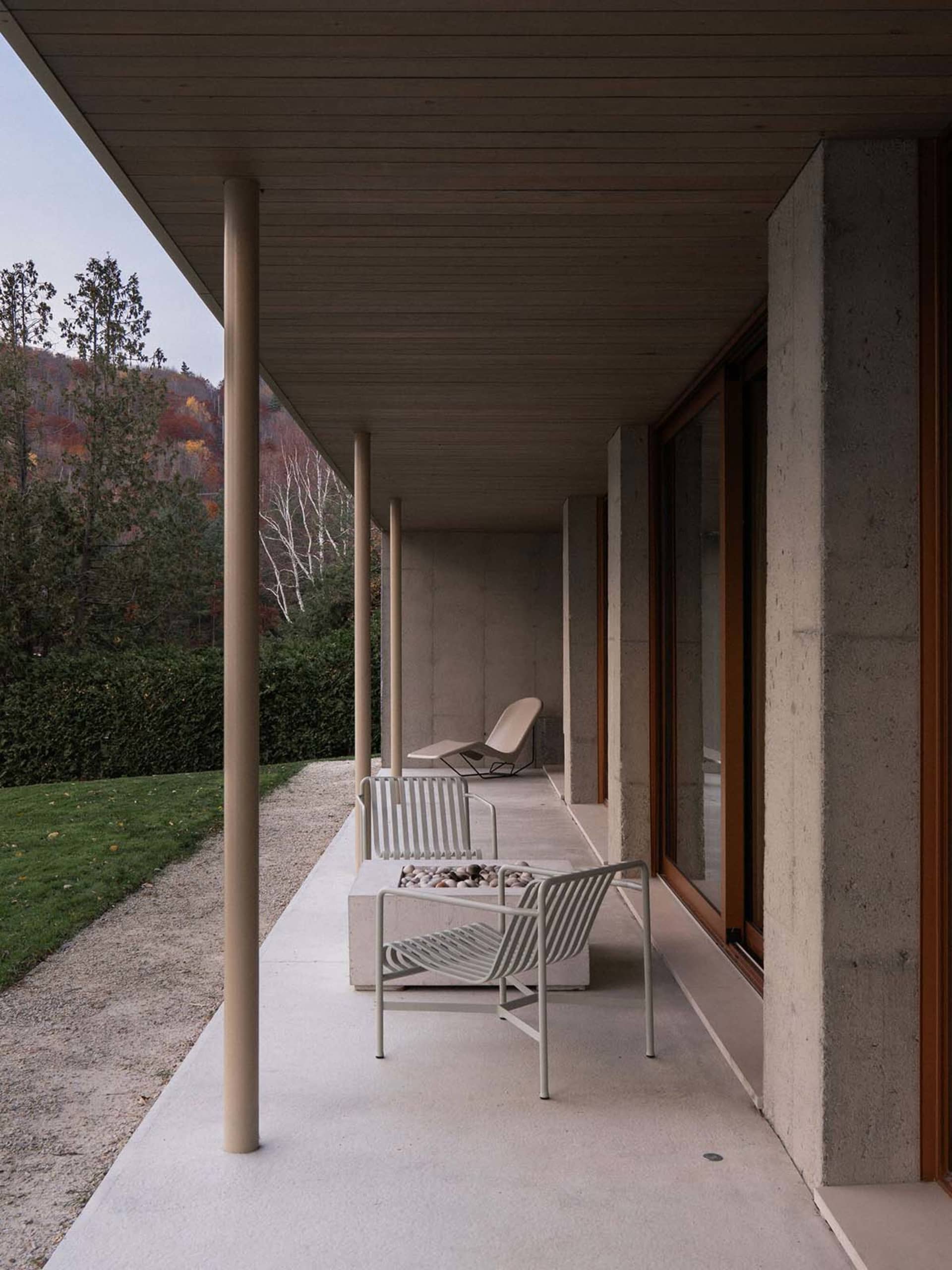 Concrete exterior of a modern building with a minimalist design, featuring a long, covered walkway with simple seating and a