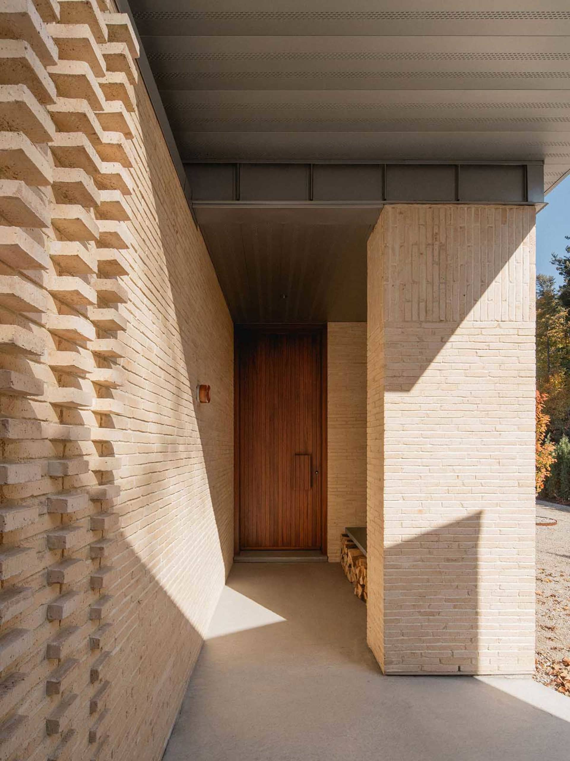 A modern building entrance with a wooden door and a textured brick wall.