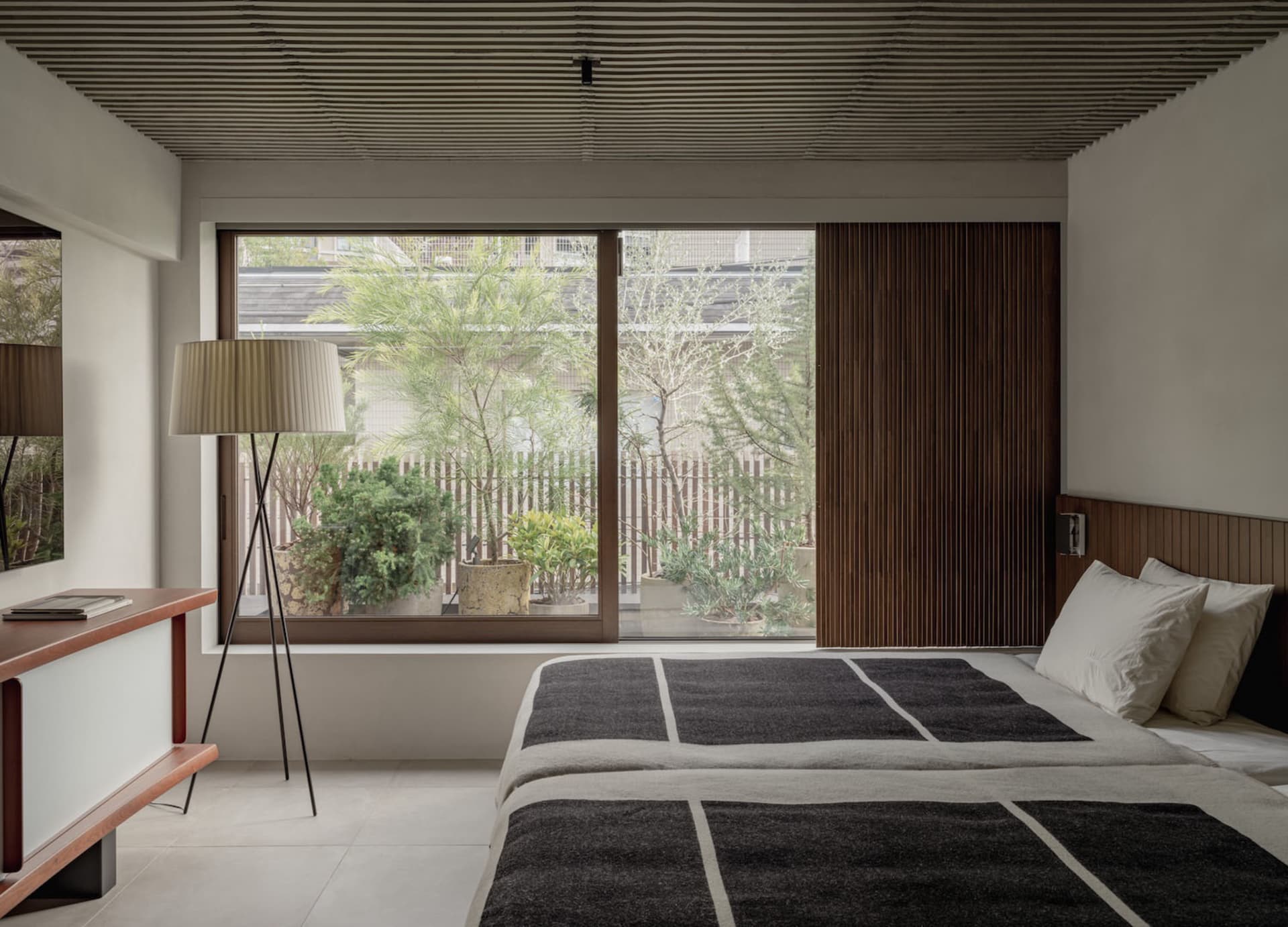 A minimalist bedroom with a large window, natural lighting, and a wooden headboard.