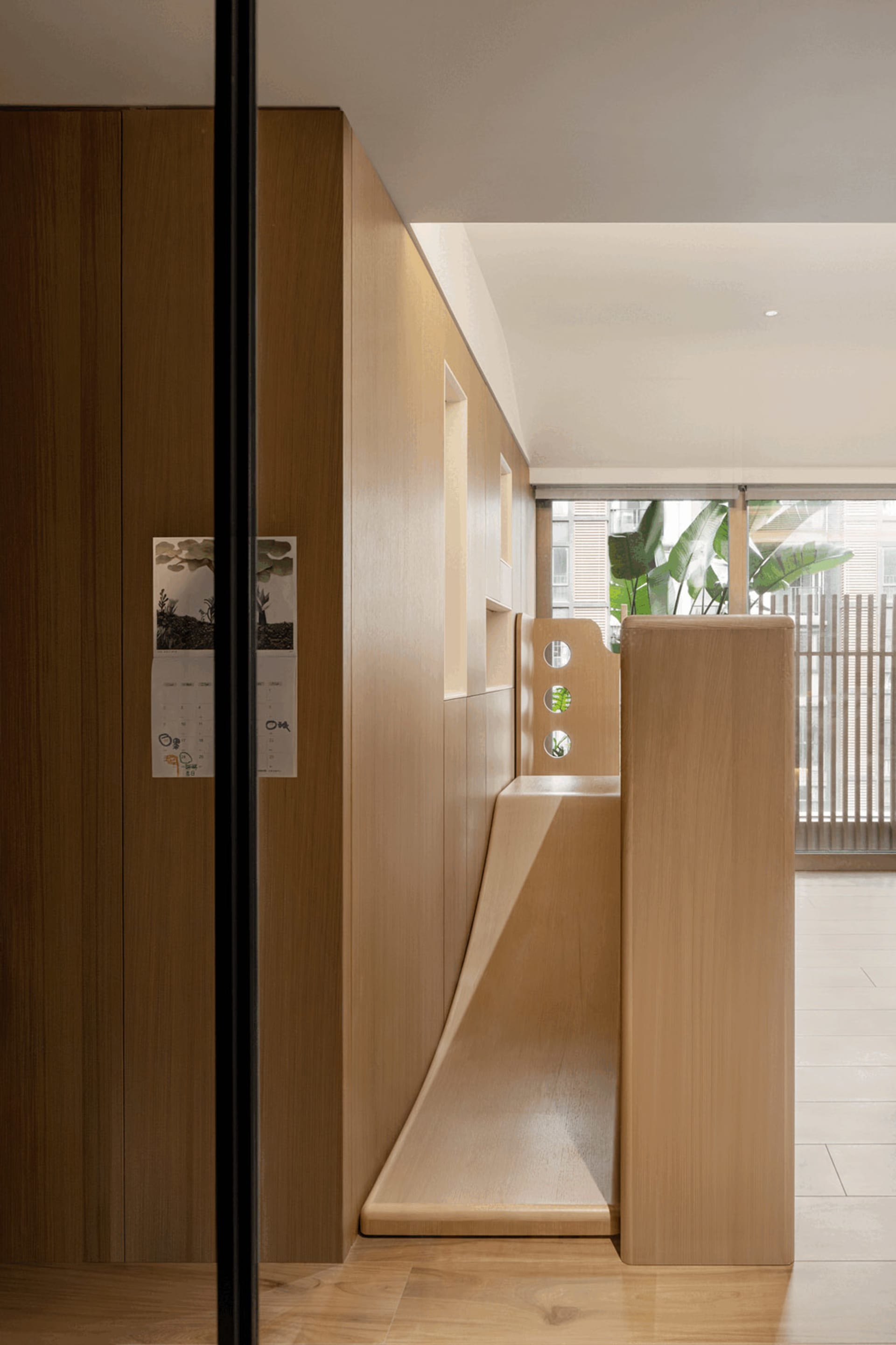 A minimalist children's play area featuring a wooden slide integrated into a wooden wall with cut-out windows.