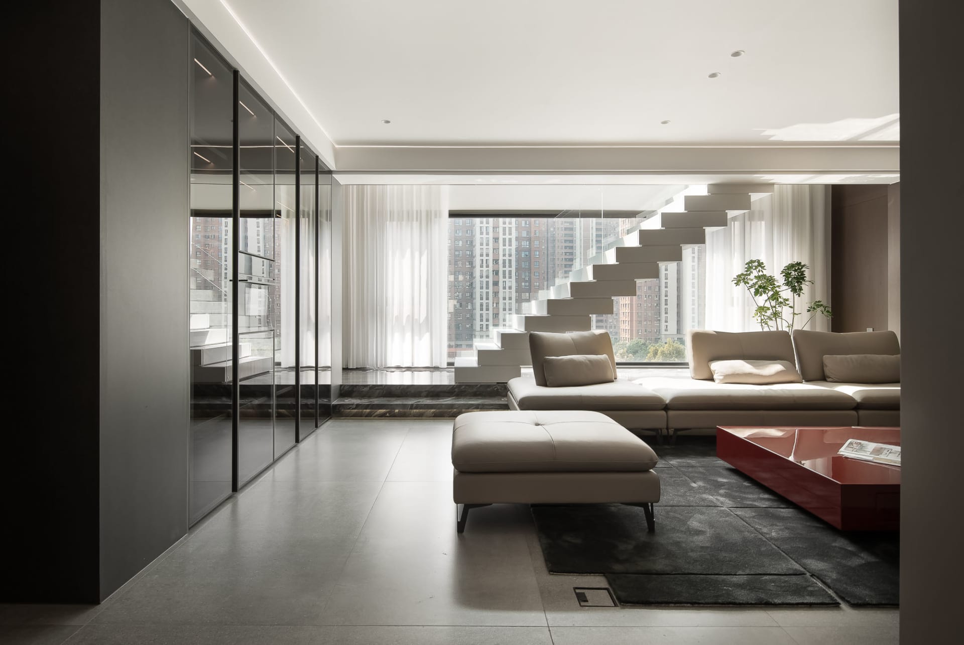A modern living room featuring concrete walls and floors, with a large white couch and a red coffee table