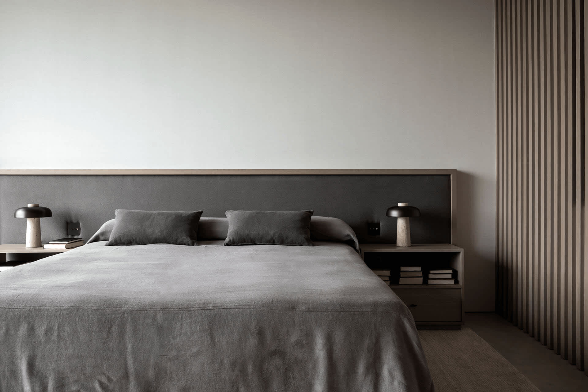 A minimalist bedroom with a gray fabric bedspread and matching pillows.