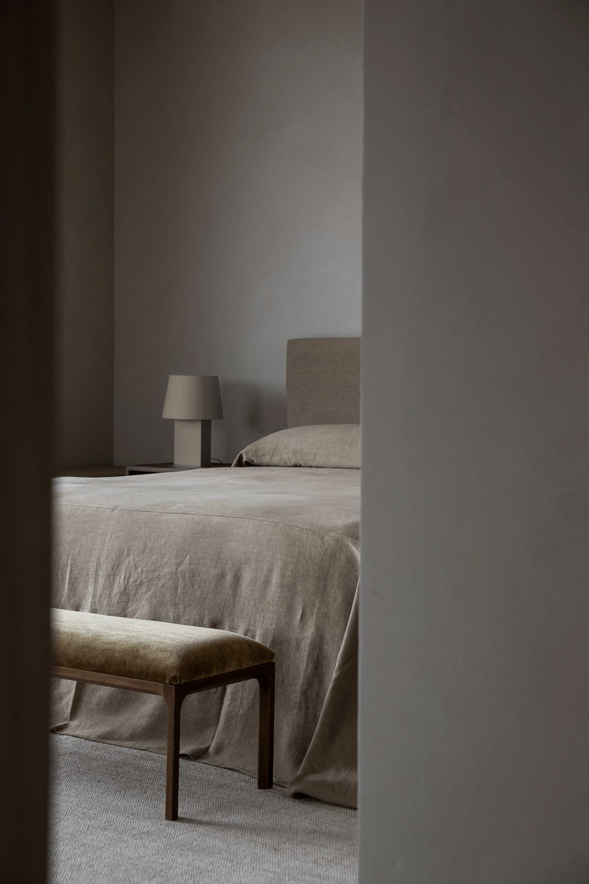 A minimalist bedroom featuring a bed with neutral-colored fabric bedding and a wooden bench.
