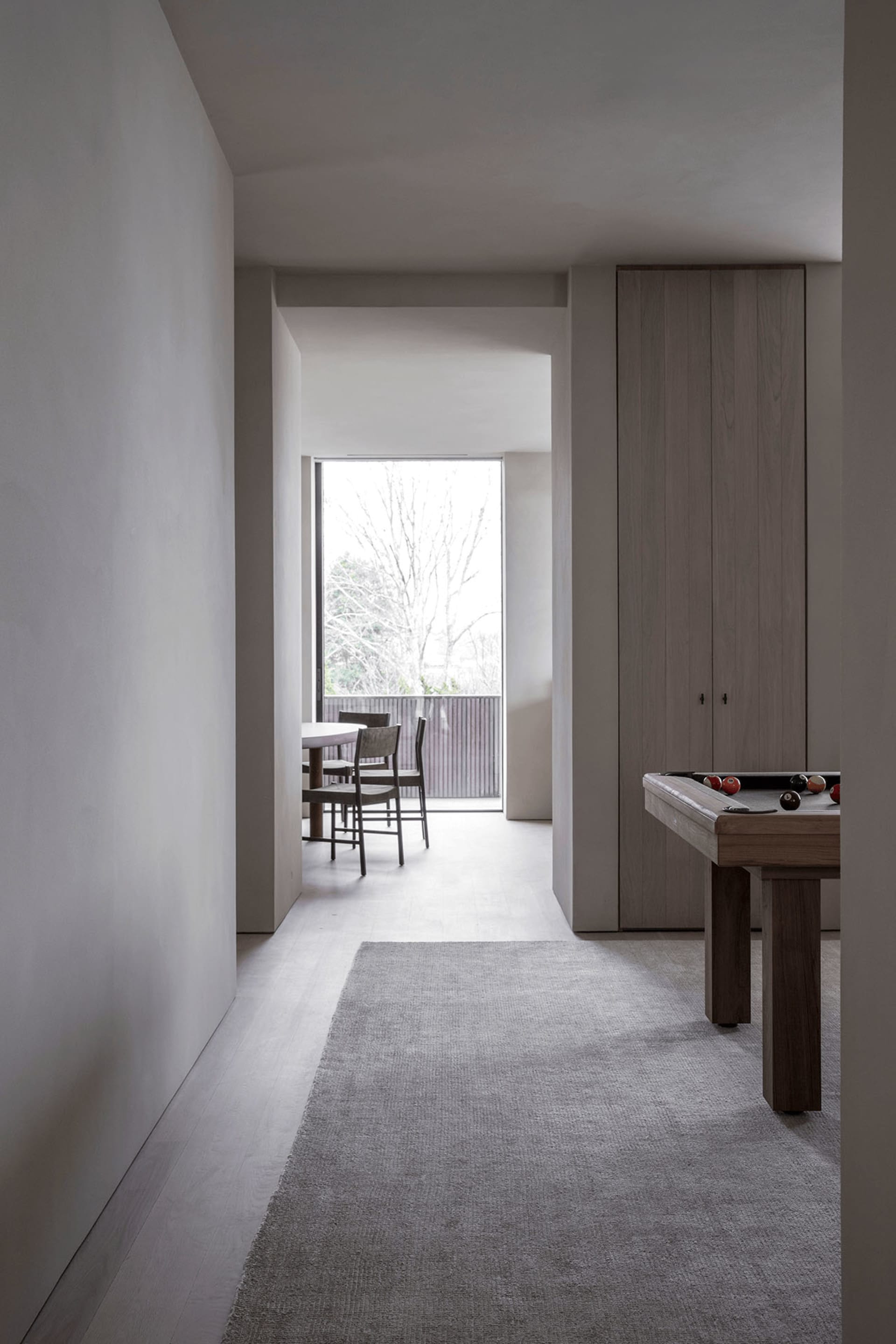 A modern minimalist living room featuring a wooden floor, minimalist furniture, and a large window with a view of trees.