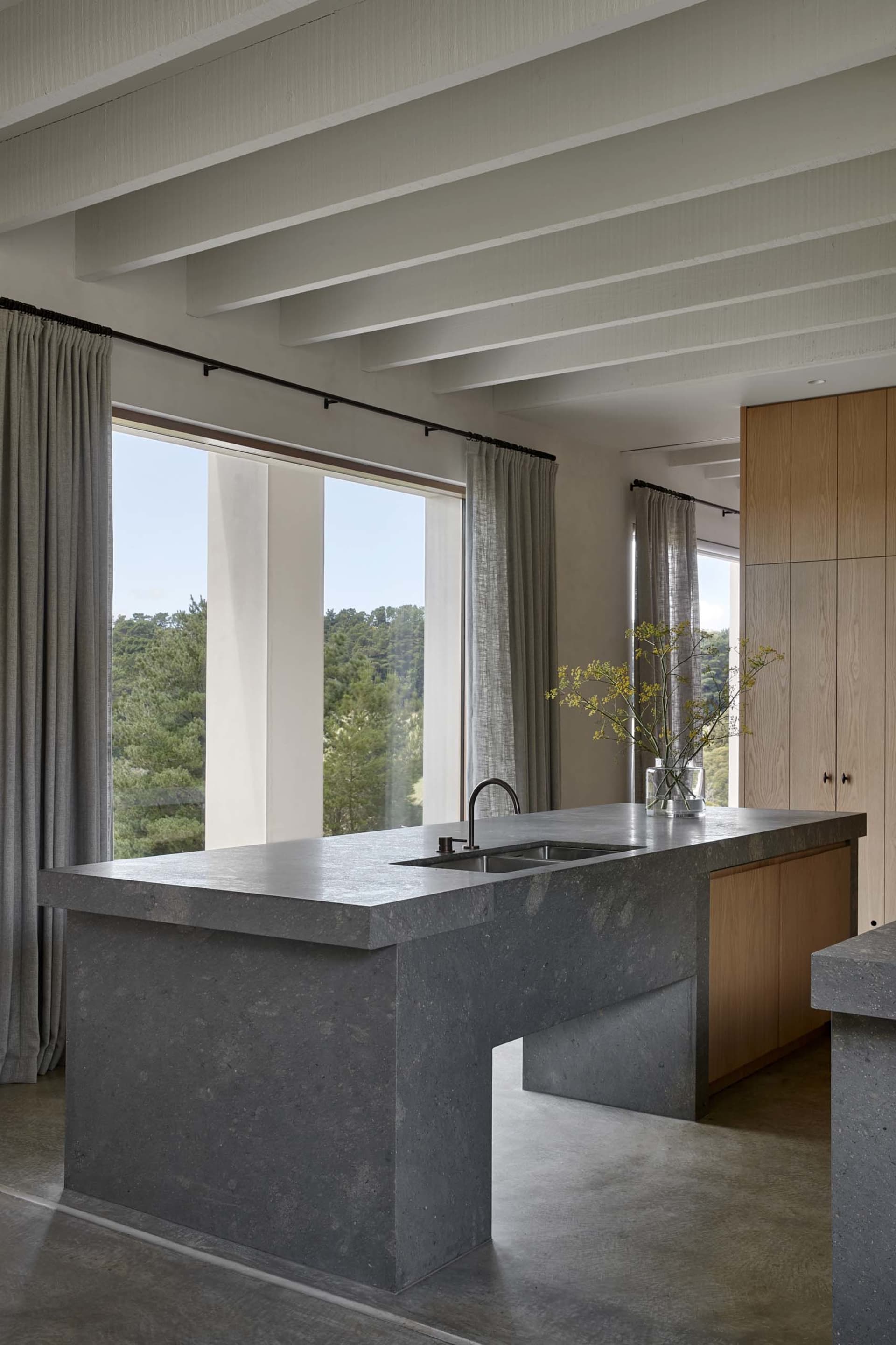 Contemporary kitchen featuring a minimalist design with concrete countertops, a waterfall island, and large windows overlooki