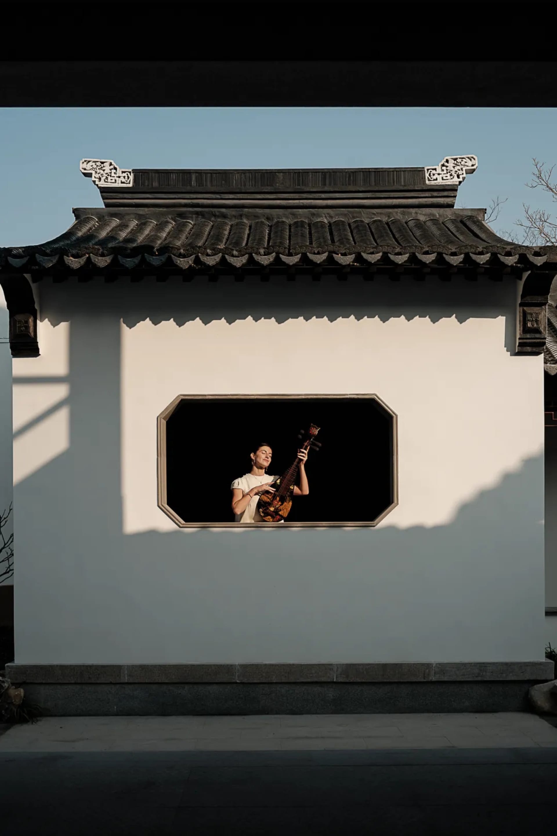 A person playing a traditional Chinese instrument in a window of an ancient building.