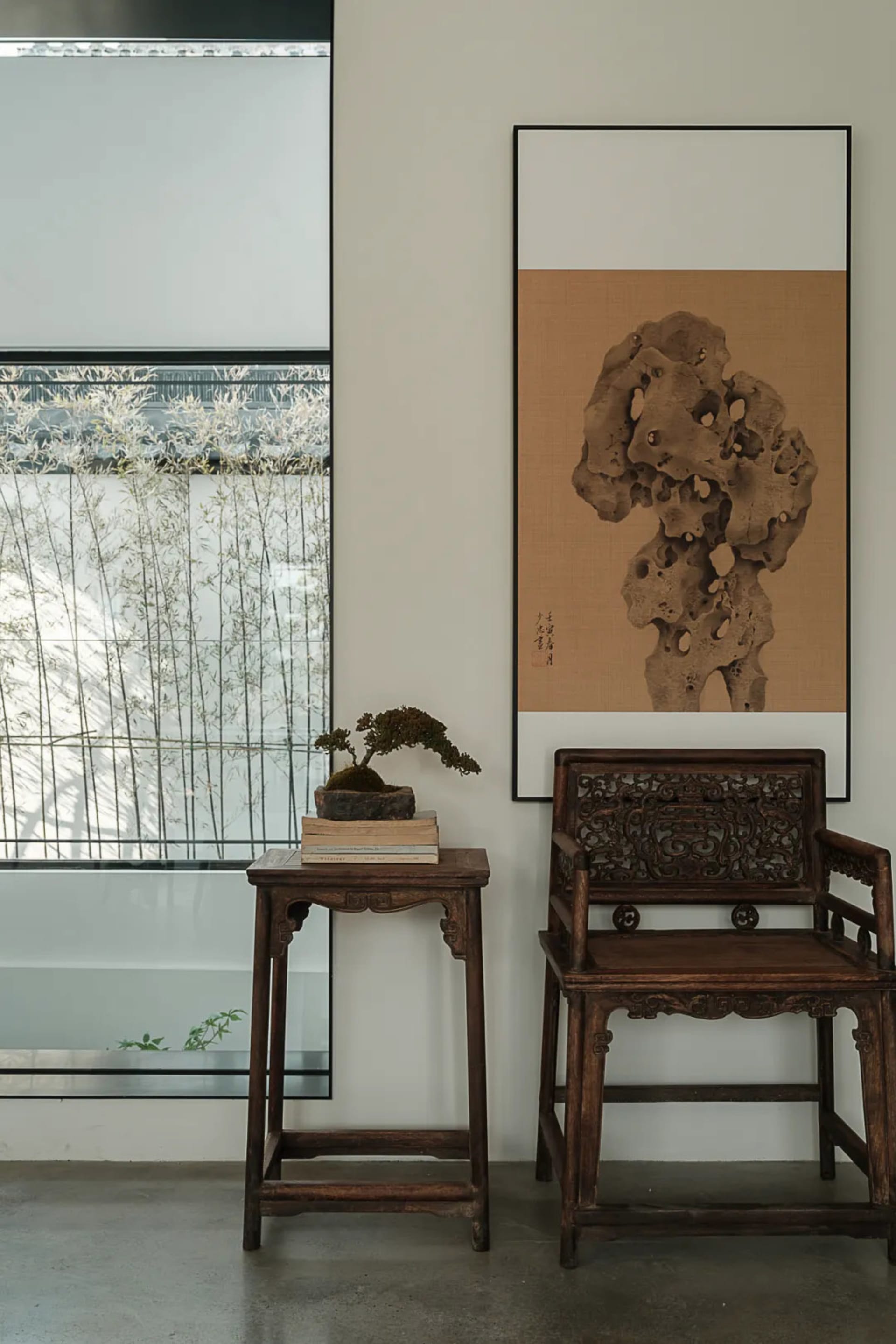 A modern living room featuring wooden furniture and stone accents, with a bonsai tree on a small wooden table and a framed ar