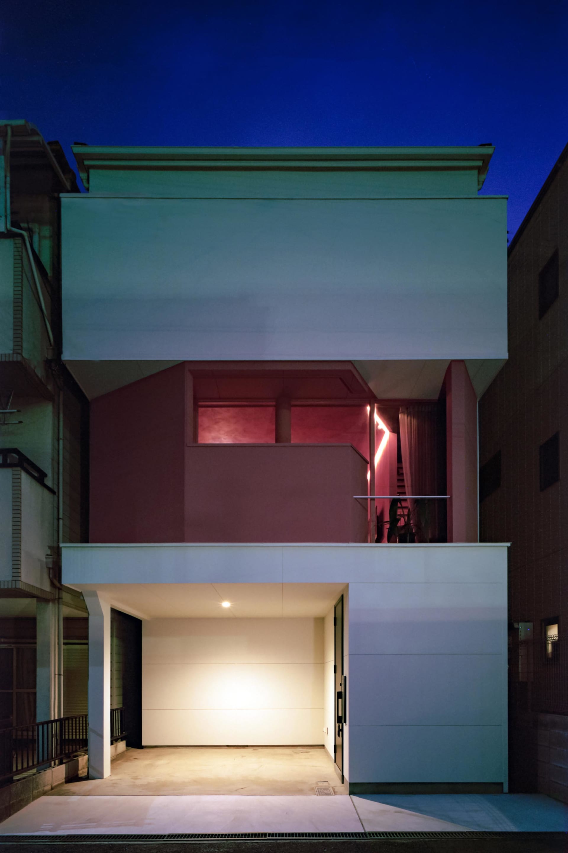 一棟現代住宅建築採用極簡設計，混凝土外牆搭配溫暖的室內燈光。
