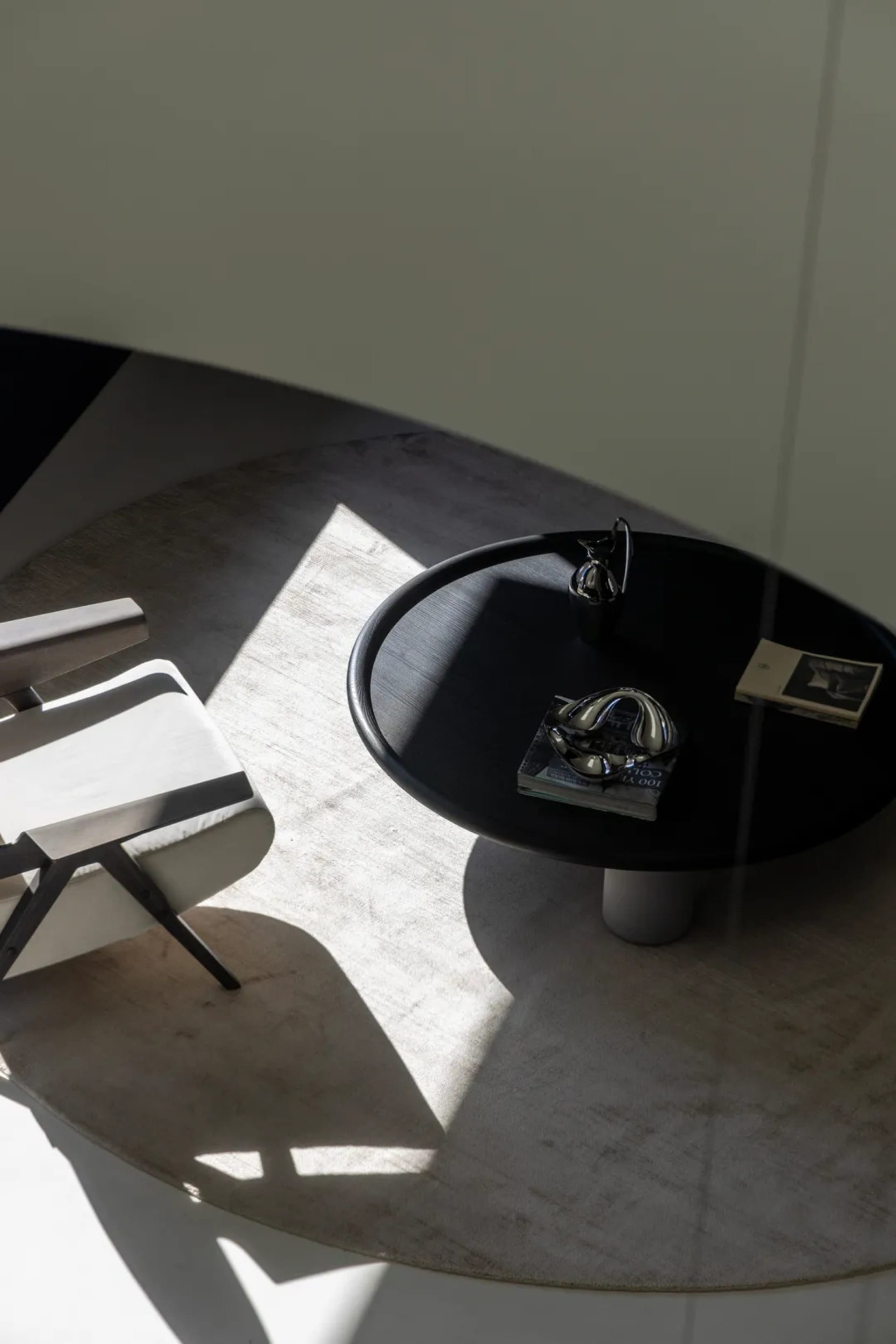 A modern living space featuring a sleek black coffee table with glass legs and marble top placed on a textured rug.