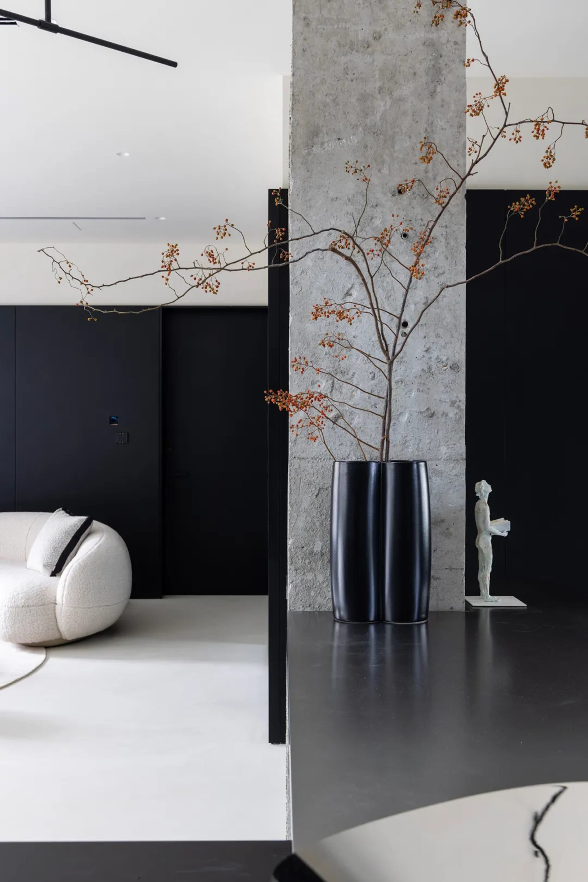 Modern living room featuring a black vase with concrete and orange berries, set against a black wall and floor.