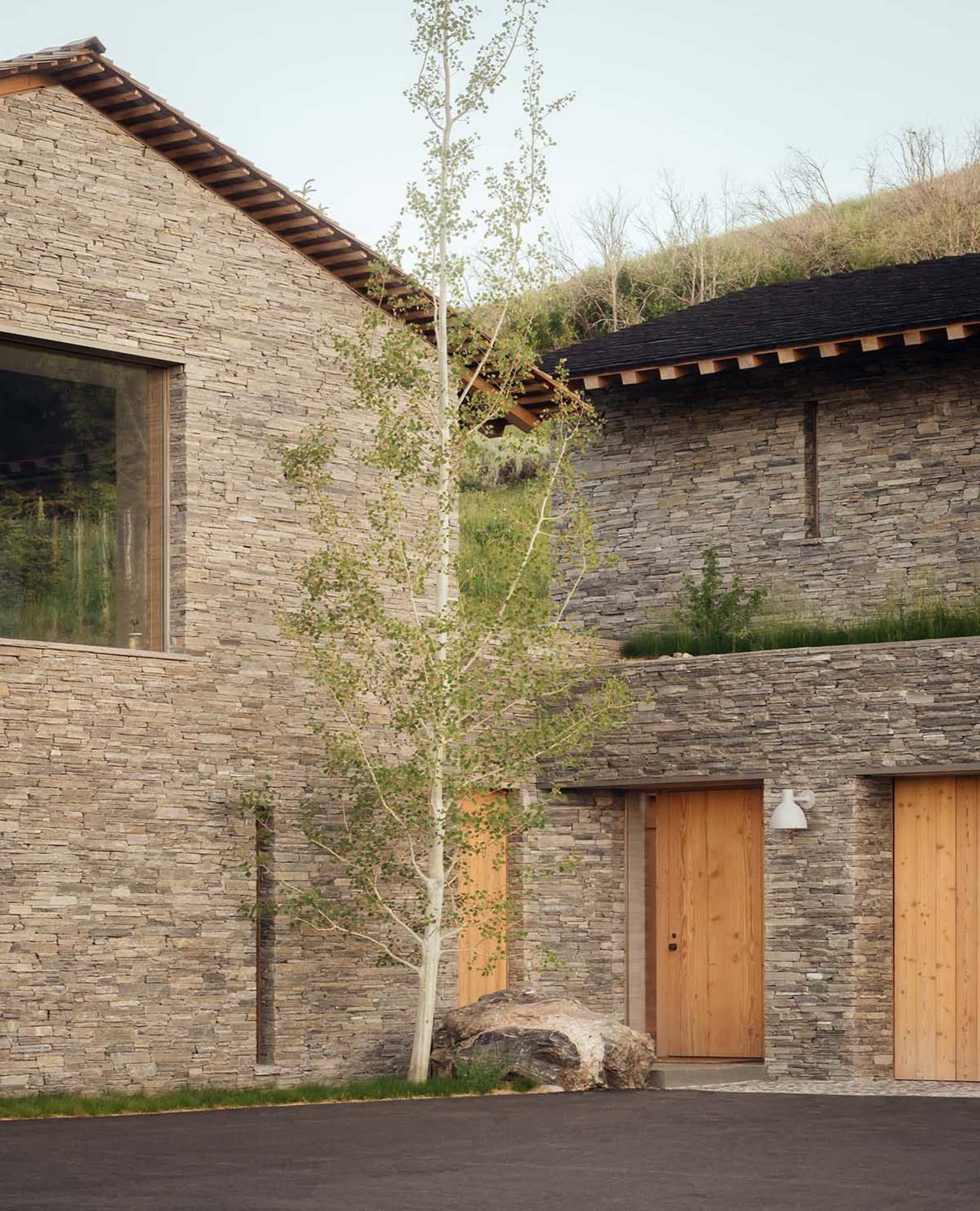 A modern residential house featuring stone walls, wooden doors, and metal accents.