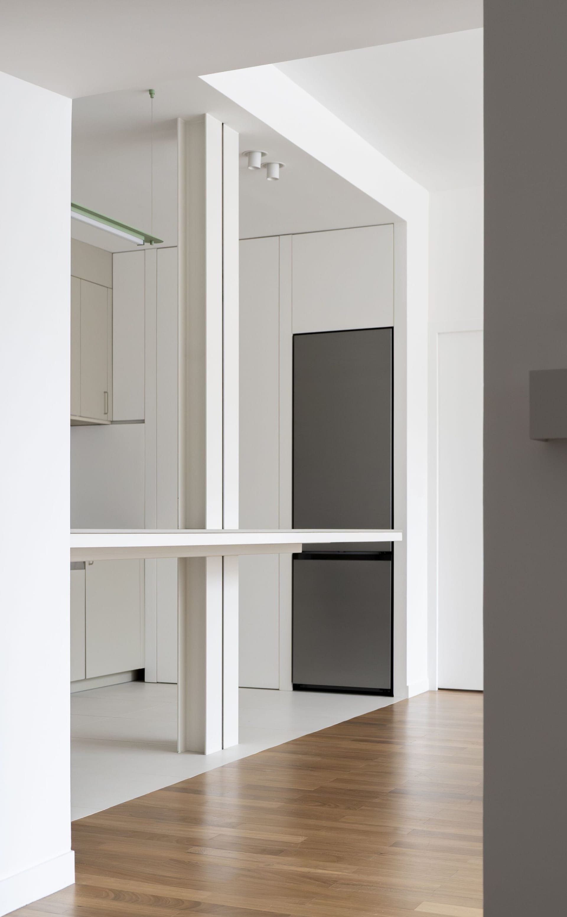 Modern, minimalist kitchen with wood paneling, featuring a sleek black refrigerator and white cabinets.