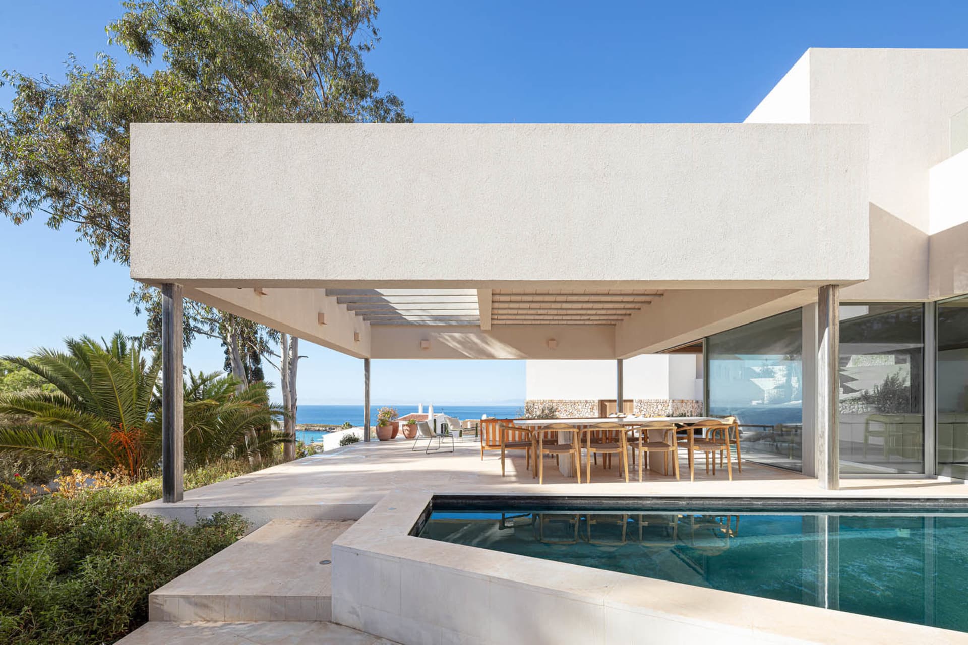 Modern outdoor dining area with concrete patio, wooden chairs, and glass table.