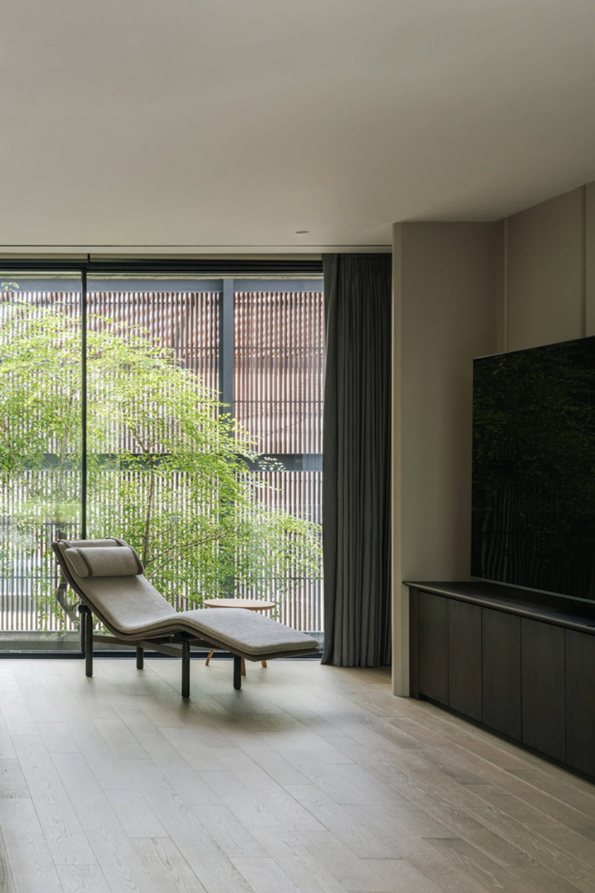 A modern living room with a lounge chair, large window, and wooden flooring.