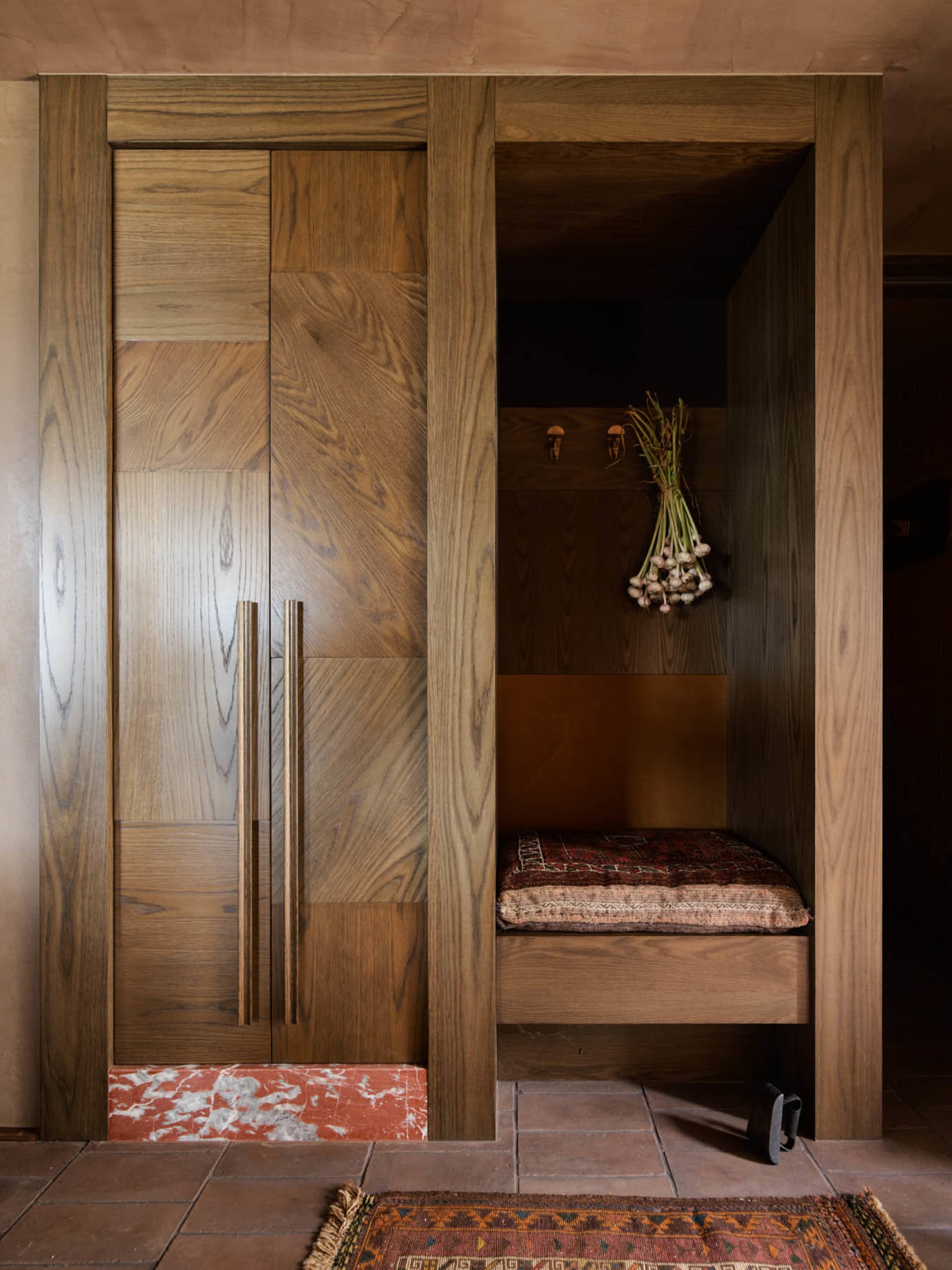 A modern wardrobe or storage nook made of oak wood, featuring a cushioned seating area and decorative onion bunch.