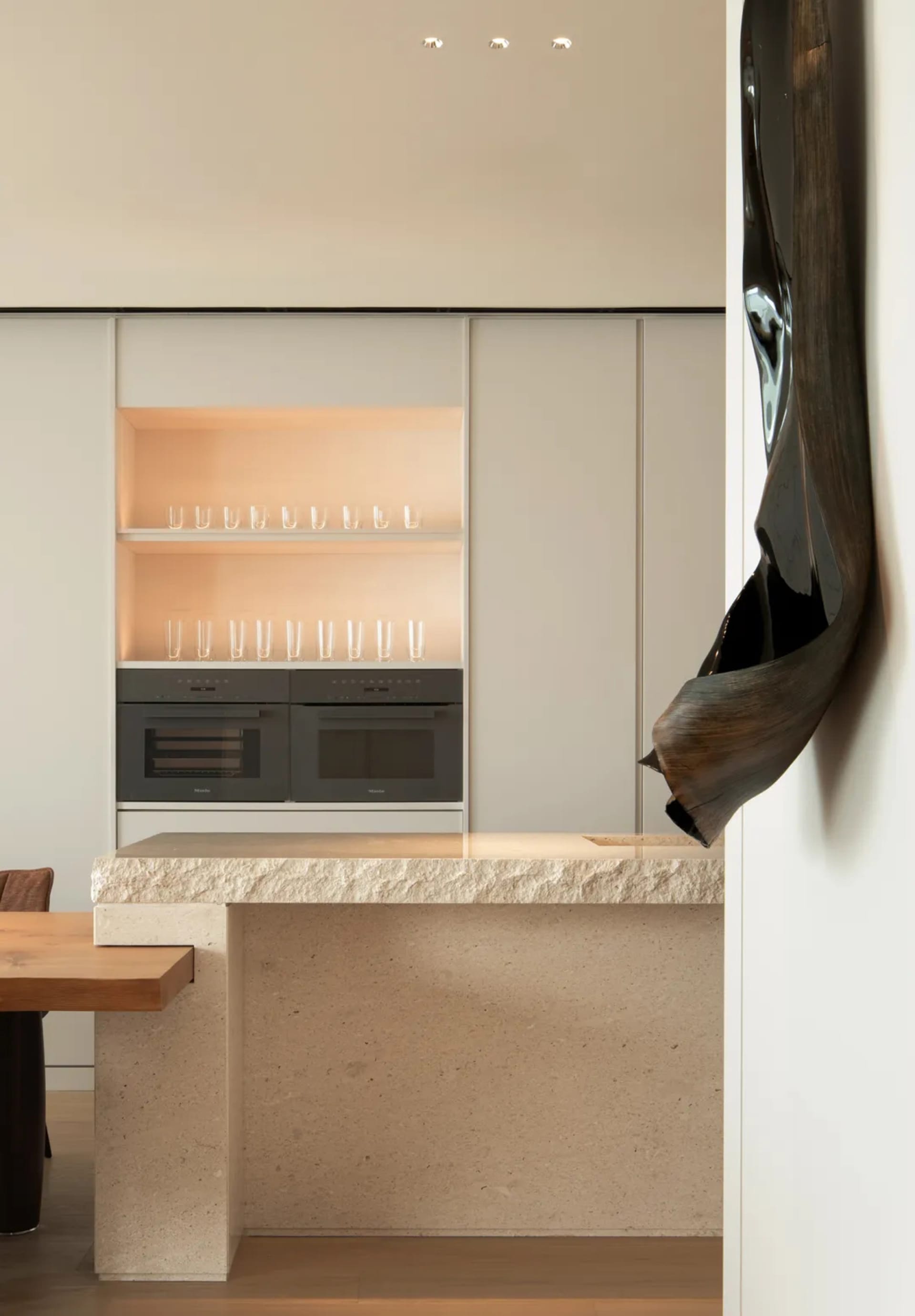 A modern minimalist kitchen with a marble countertop, illuminated cabinets, and integrated appliances.