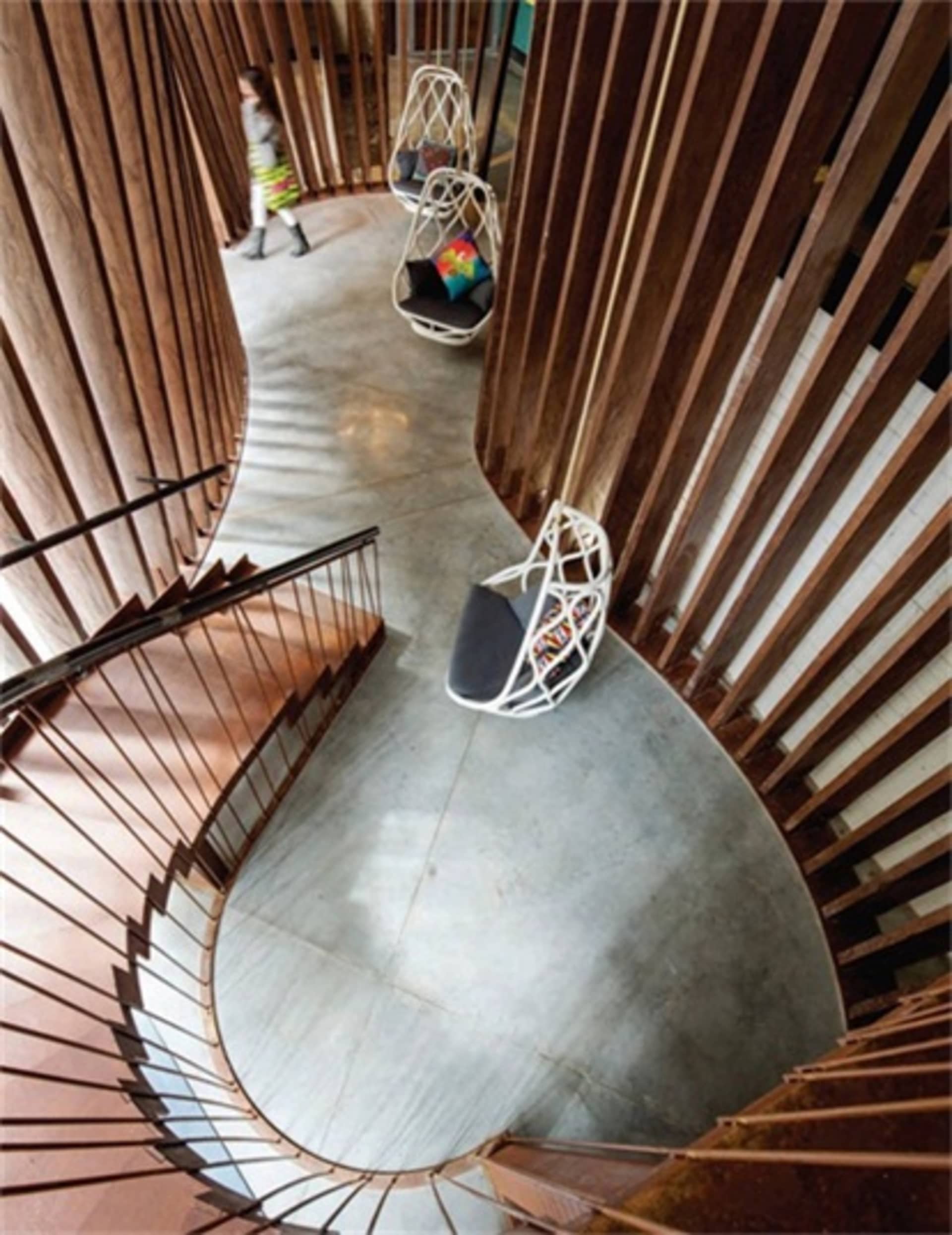 A modern lounge area with wooden floors, spiral stairs, and hanging rattan chairs.