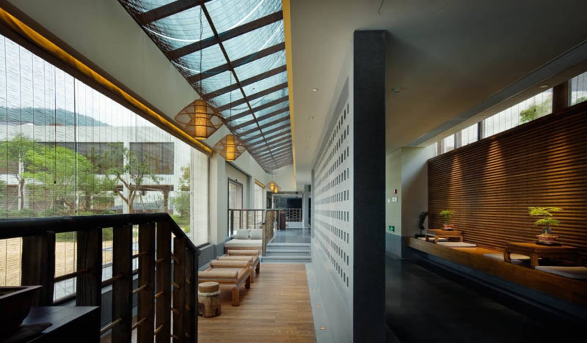 A modern, minimalist lobby with glass walls, wooden benches, and pendant lights.