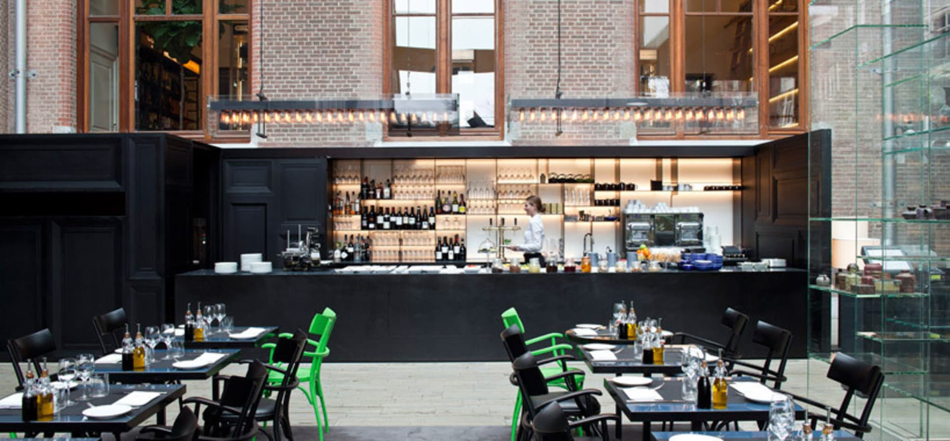 A modern restaurant interior featuring black and green accents, with a bar, tables, chairs, and a glass display case.