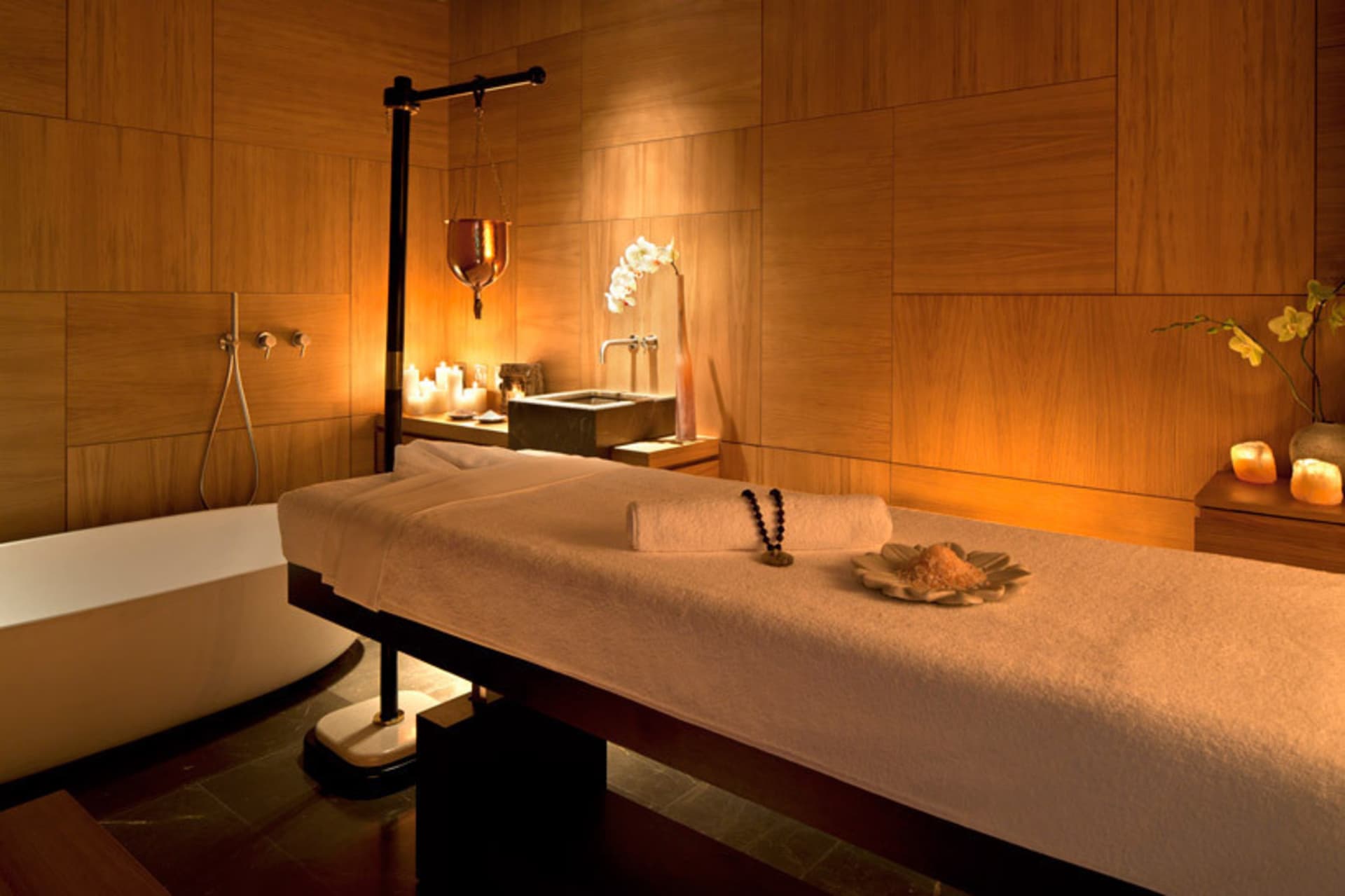 A serene spa massage room with wooden furniture, candles, and orchids, creating a peaceful atmosphere.