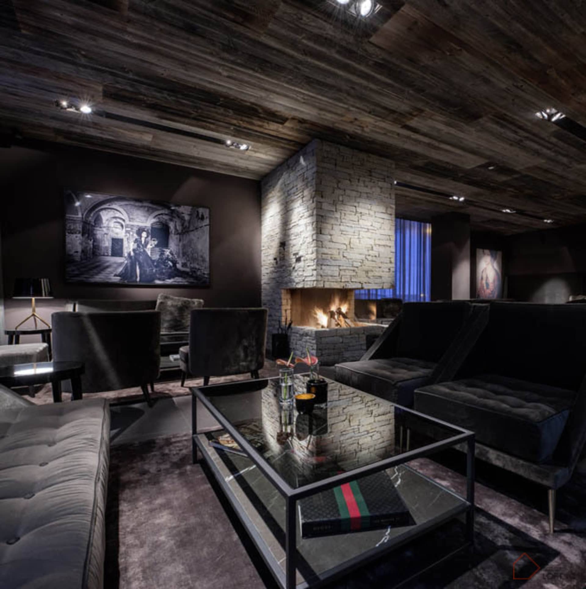 A dark, industrial-style living room with wooden ceiling, stone fireplace, and modern furniture.