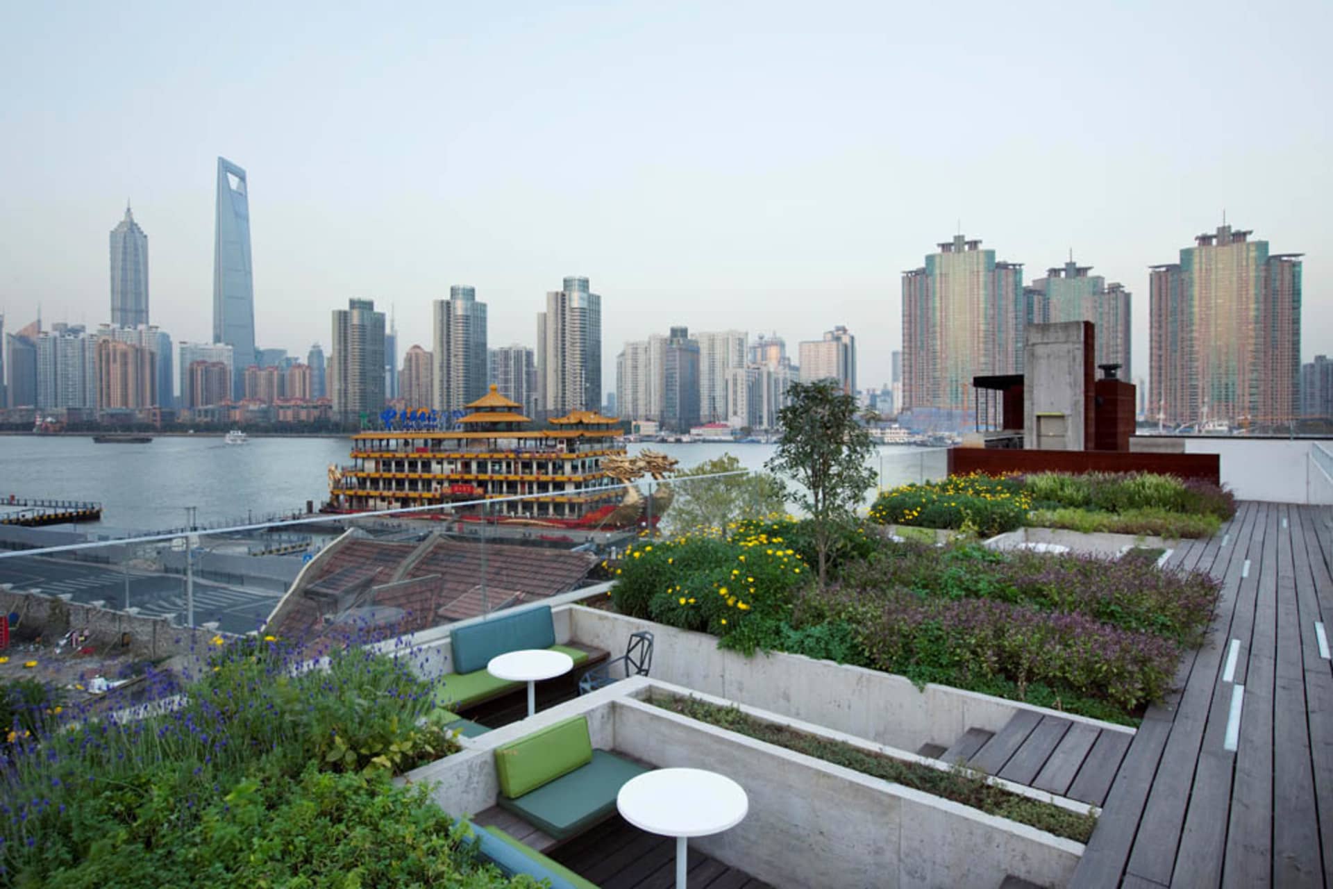 Urban rooftop garden with concrete planters and seating areas overlooking a city skyline.