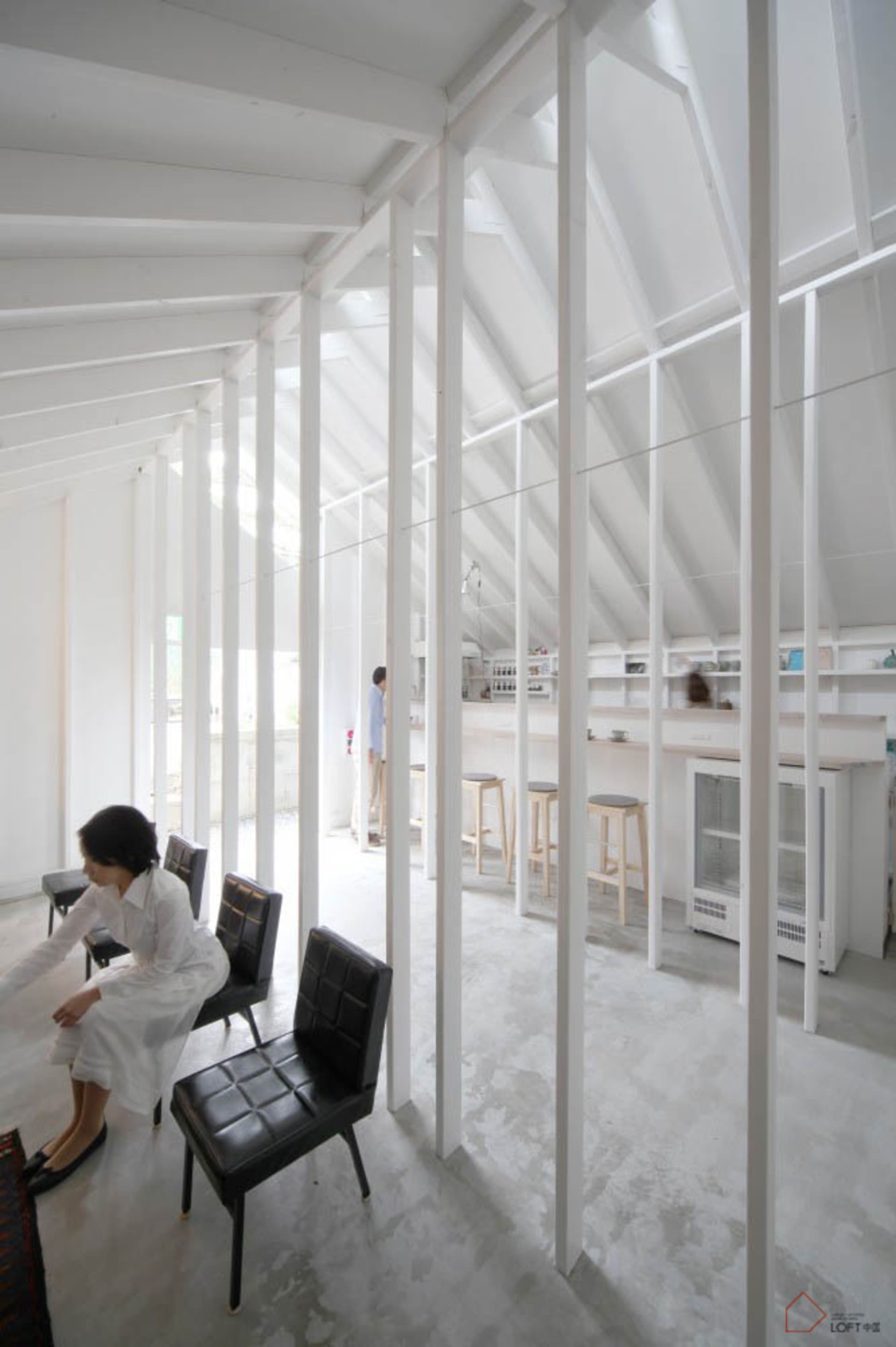 Interiors of a minimalist white space featuring concrete flooring and furniture.