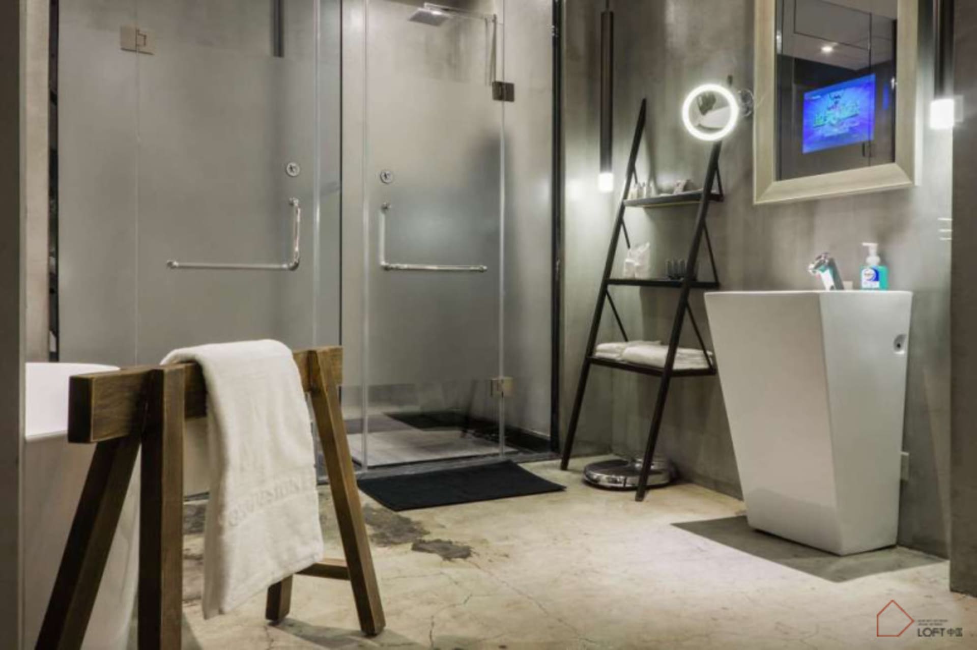 Industrial-style bathroom featuring glass shower enclosure, metal ladder shelf, concrete floor, and metallic sink with televi