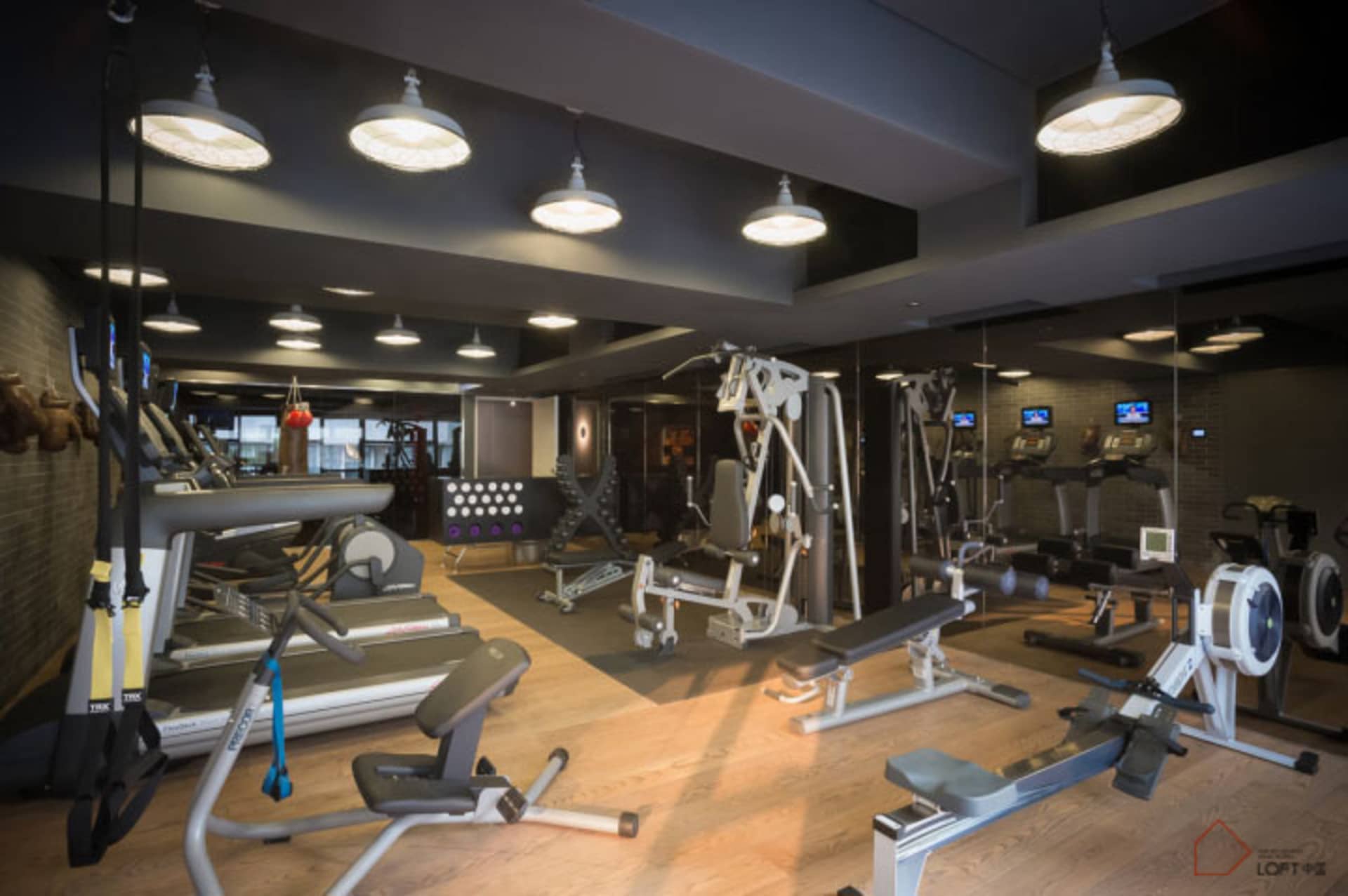 A modern, industrial-style fitness center with metallic equipment and laminate flooring.