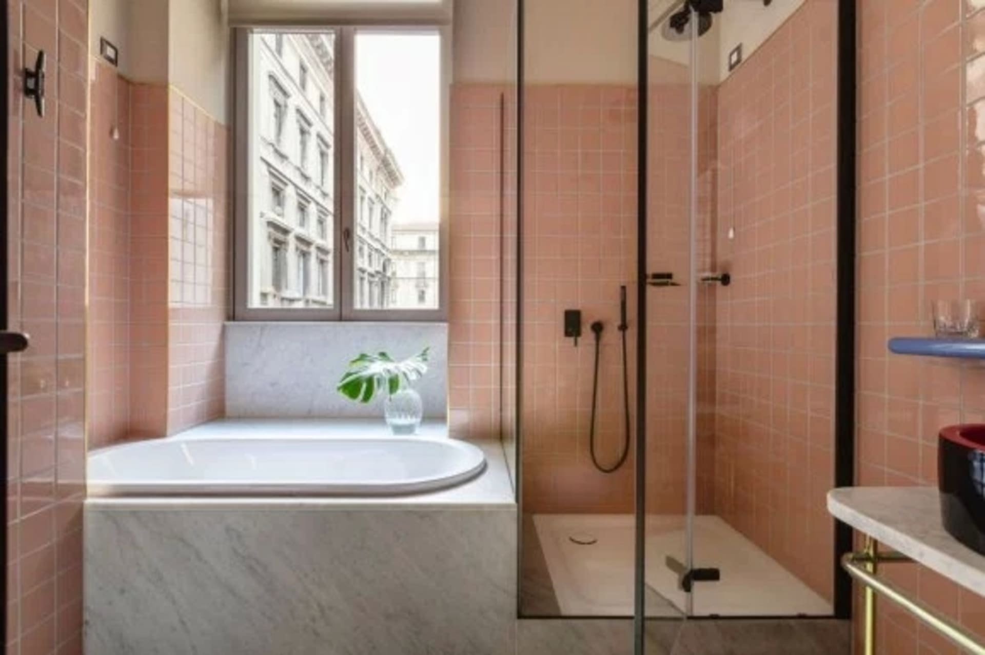 A modern bathroom featuring marble, pink tiles, and a view of the city.