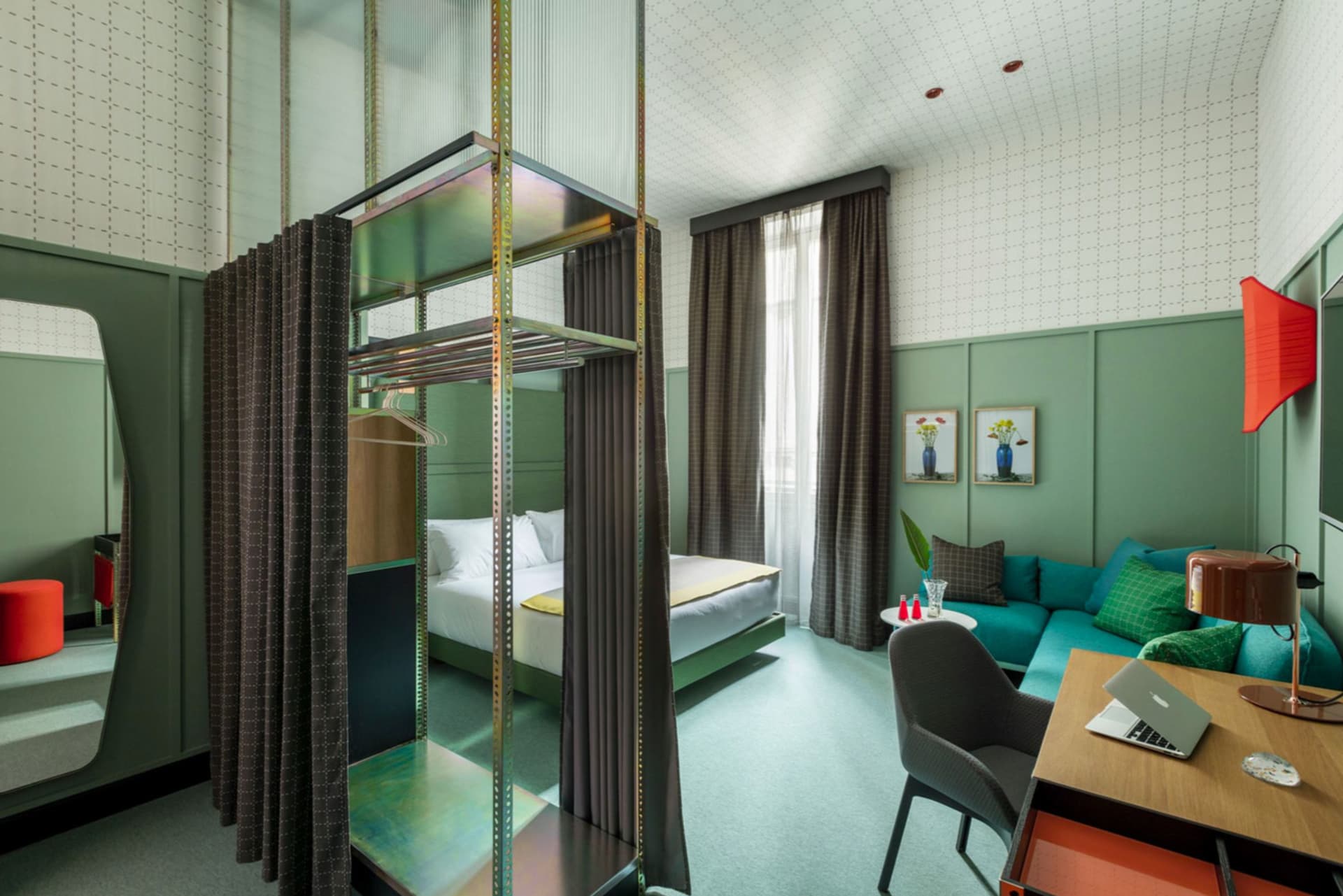 A modern hotel room featuring green paneling, curtains, and wooden furniture.