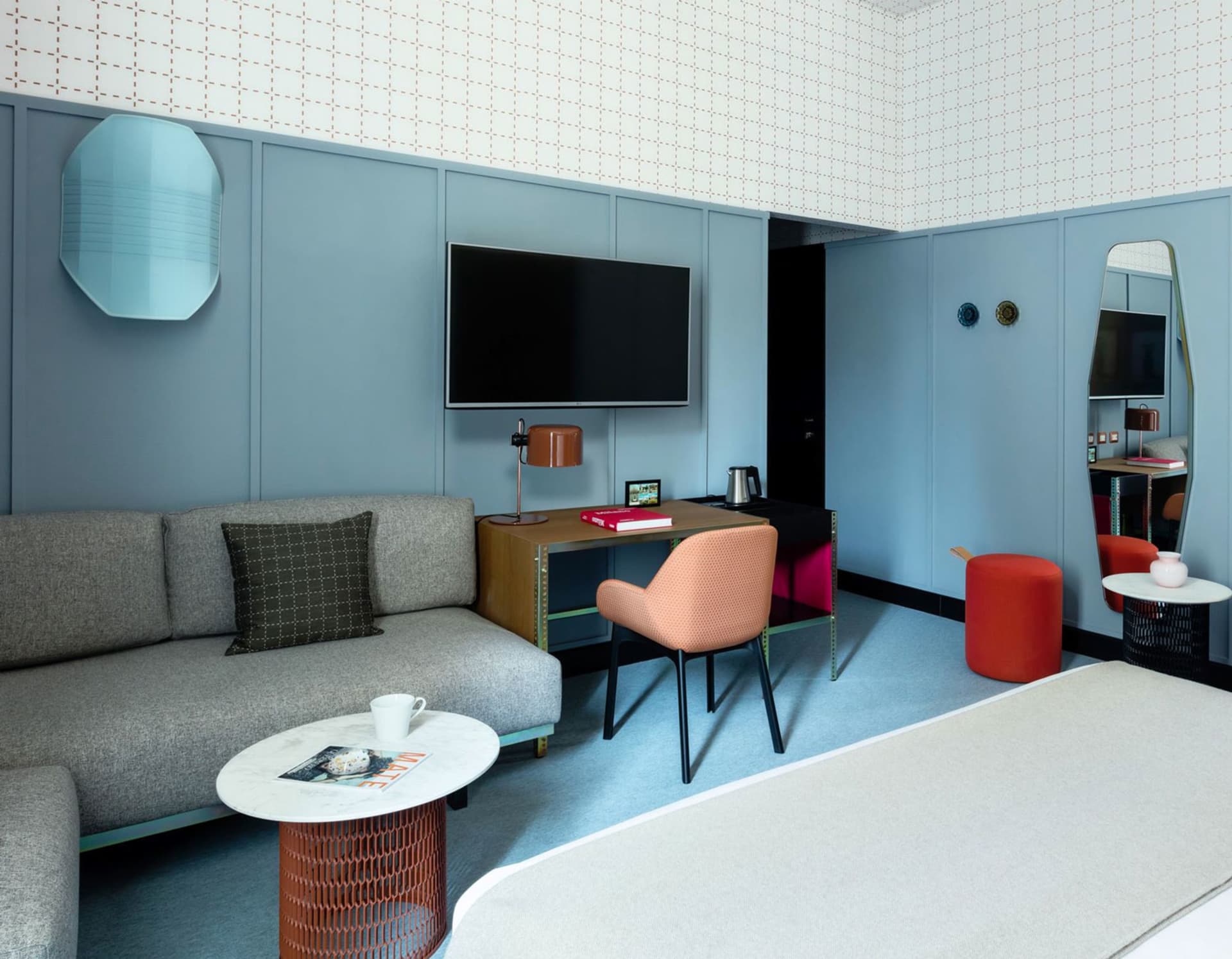 A modern hotel suite featuring a comfortable sofa, a flat-screen TV, a desk with a chair, and a coffee table with a magazine
