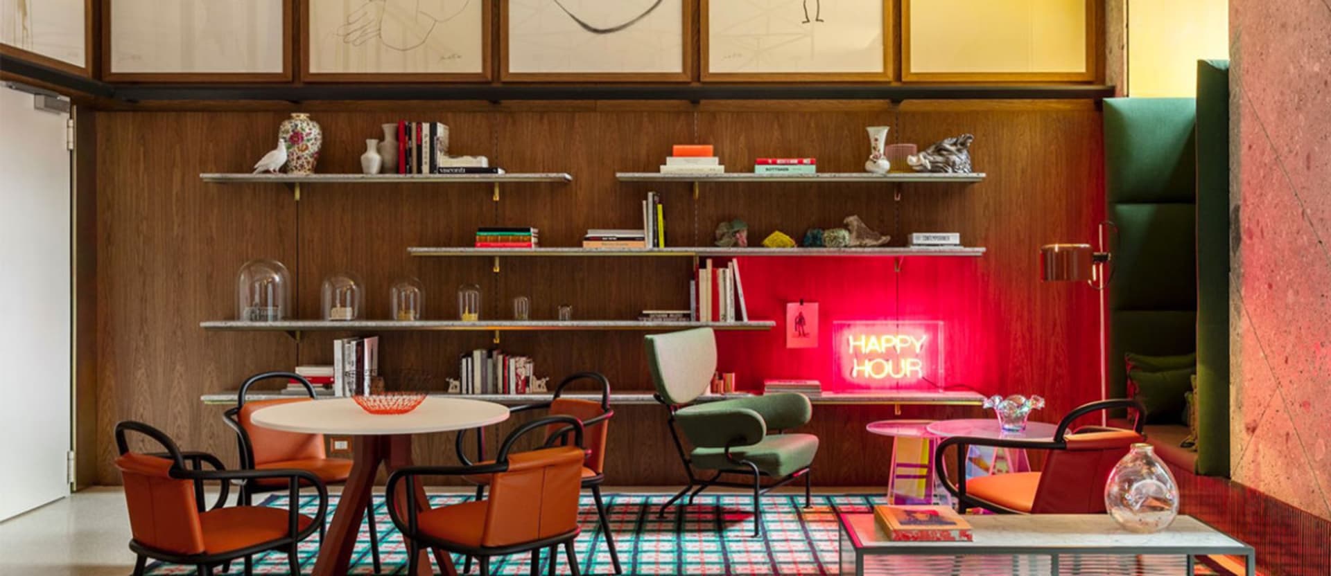 A modern restaurant interior featuring wooden walls and shelves, leather chairs, and a neon sign saying 'Happy Hour'.