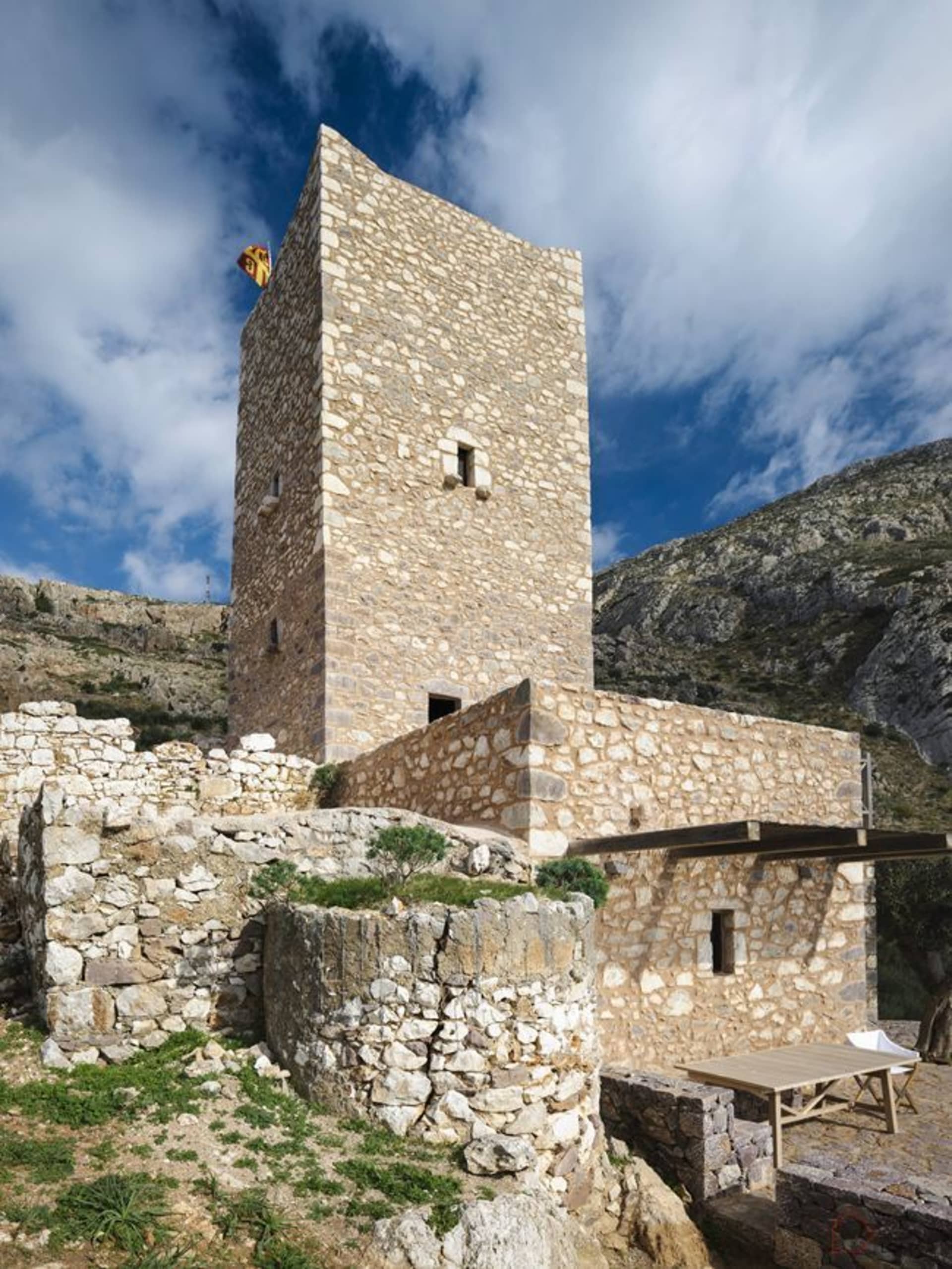 A medieval stone tower with a flag on top, set against a mountainous backdrop.