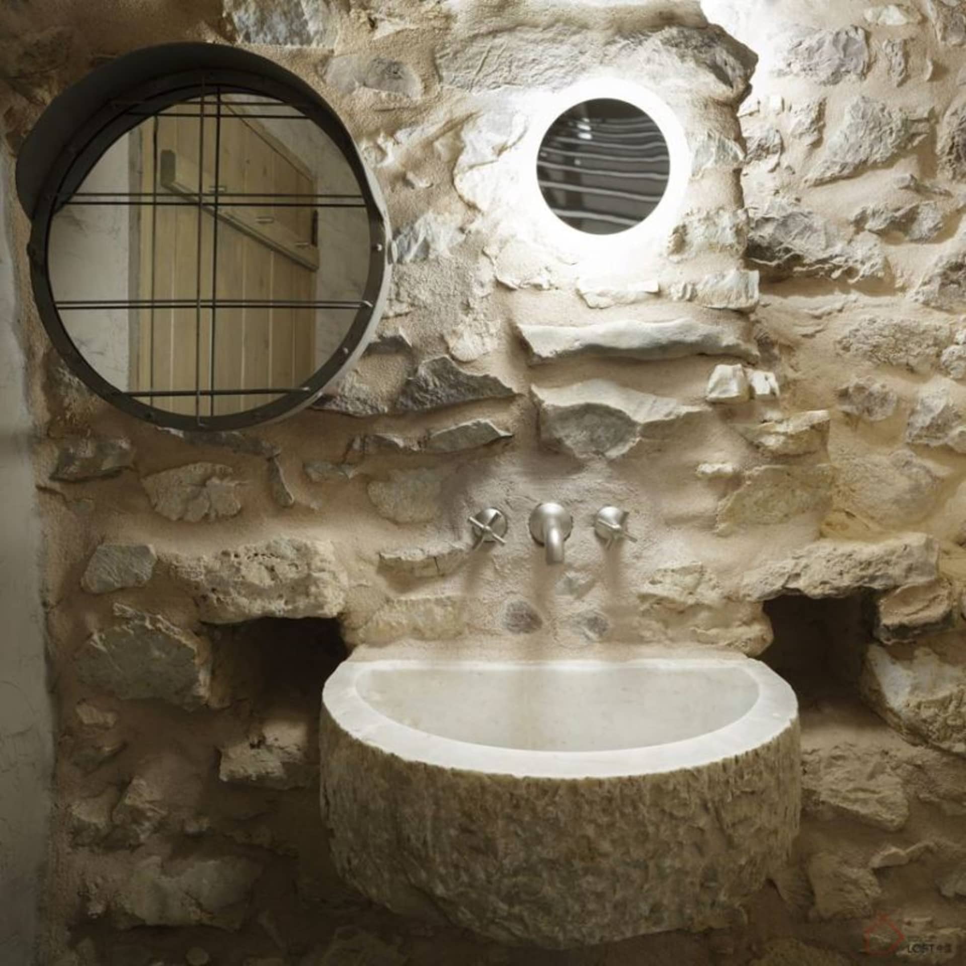 A minimalist bathroom with a stone wall, sink, and round mirror.