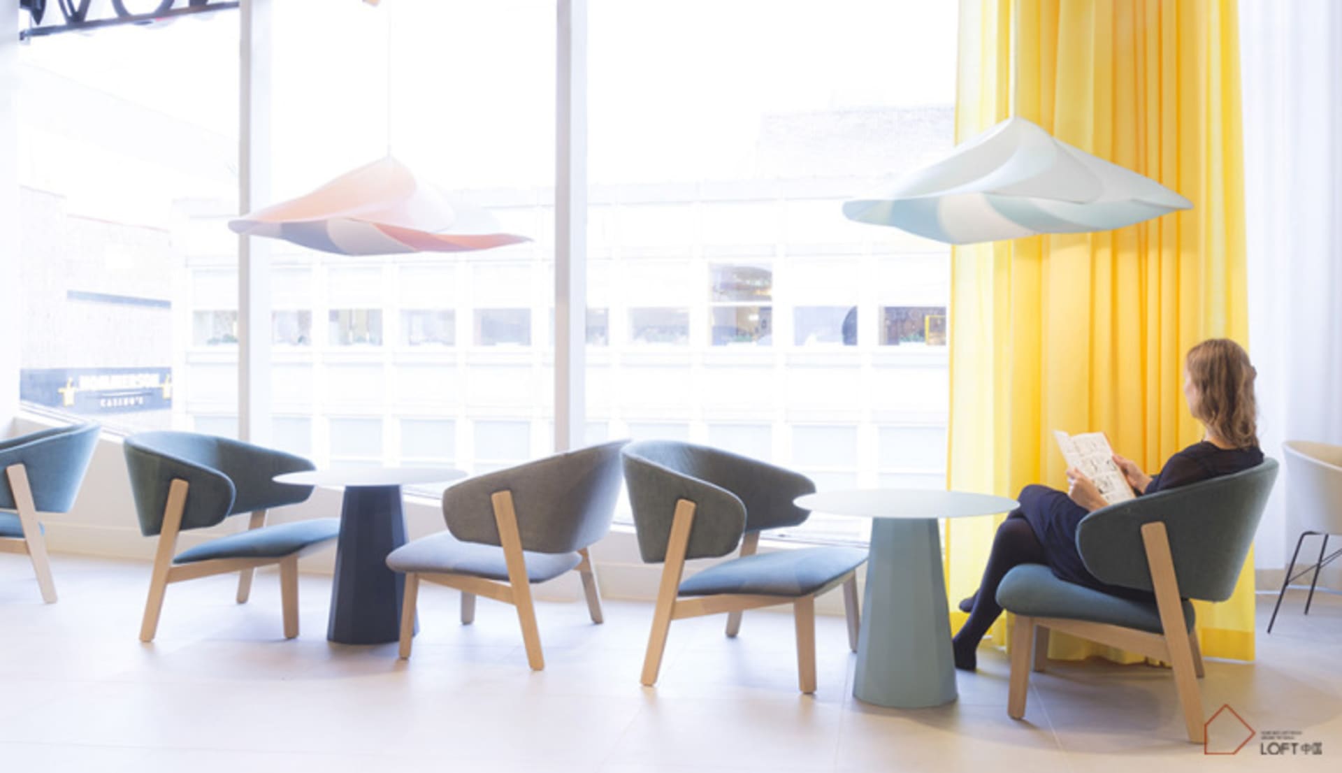 Modern, minimalist office lounge featuring sleek, contemporary seating and colorful hanging lamps.