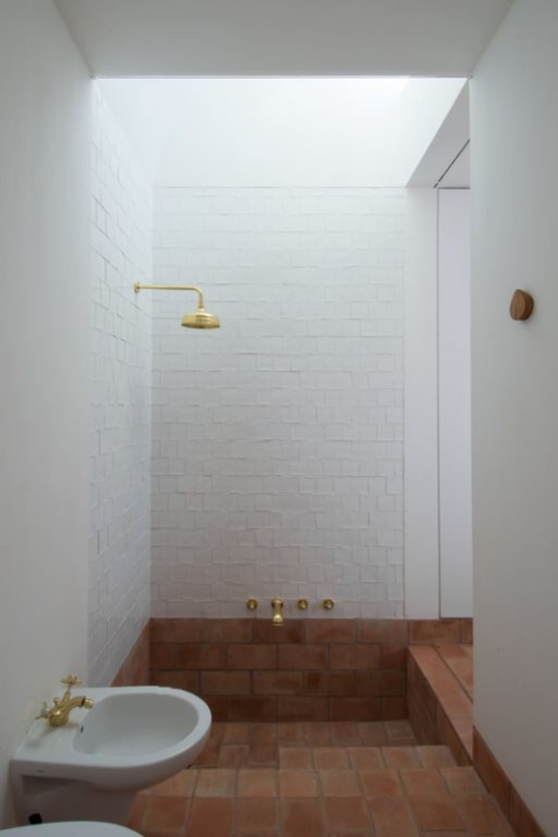 Modern bathroom with brick walls and a white sink under a golden shower faucet.