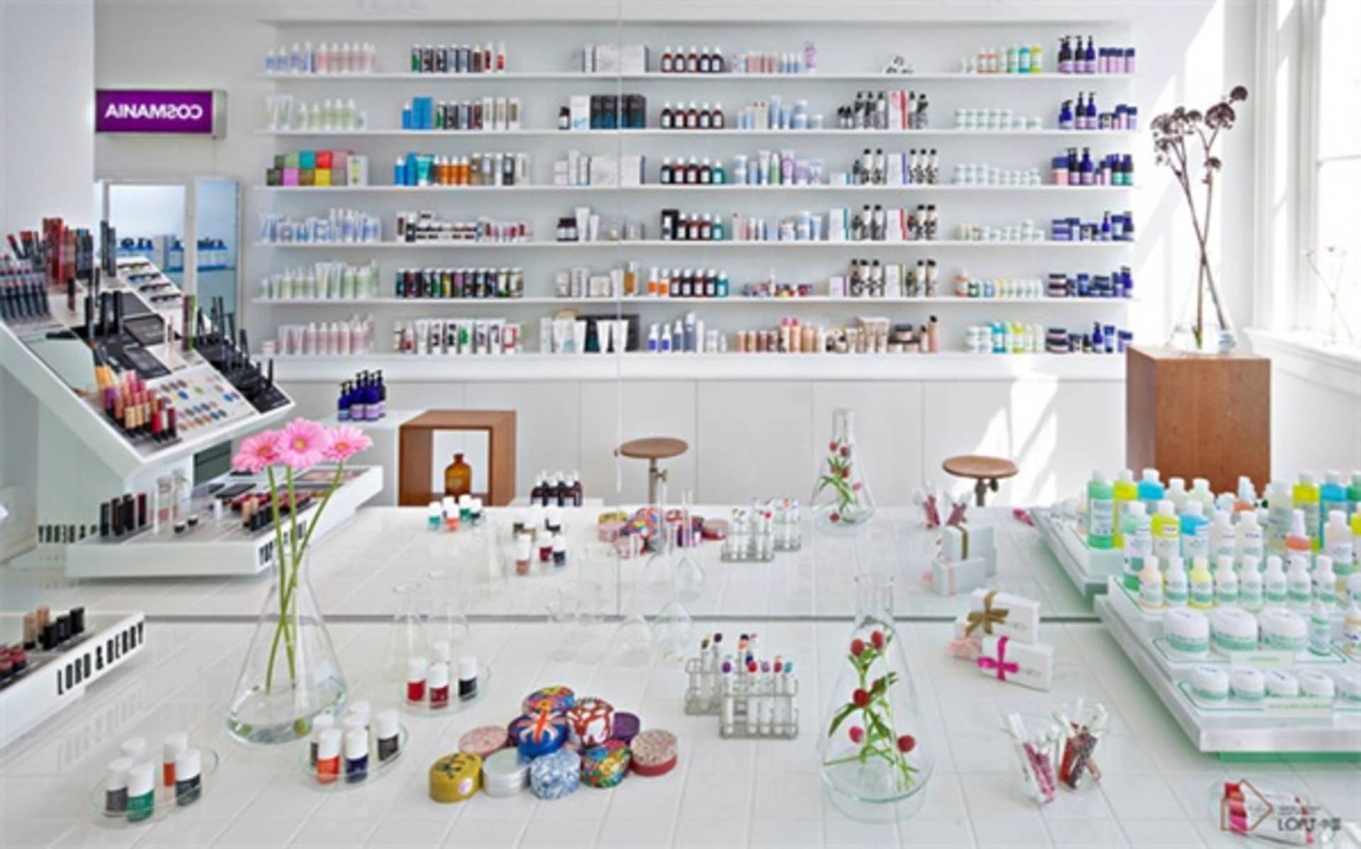 Modern, white, glass-and-metal cosmetics store interior with shelves filled with bottles and jars.