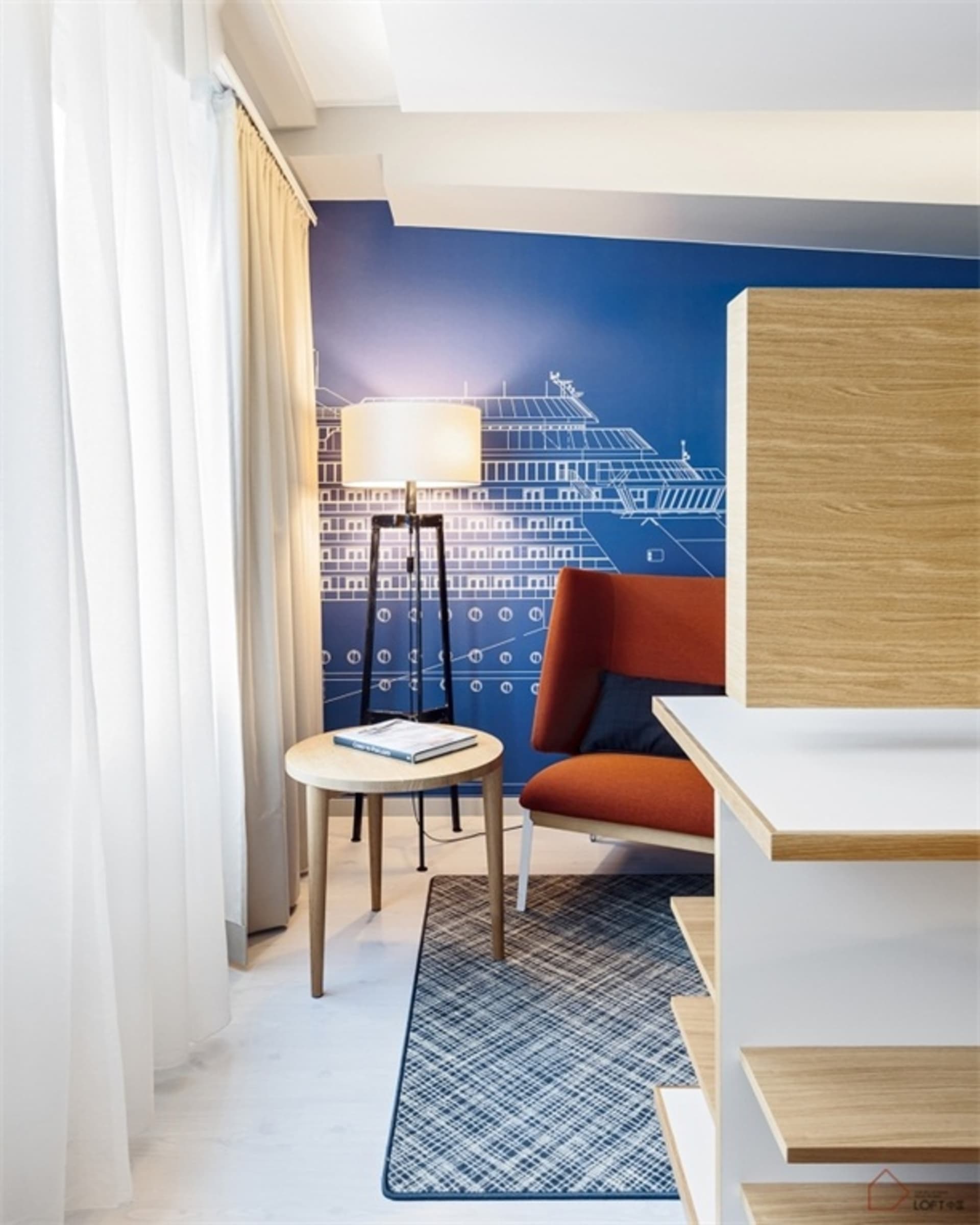 A modern hotel room featuring blue walls, wooden furniture, and a metal lamp.