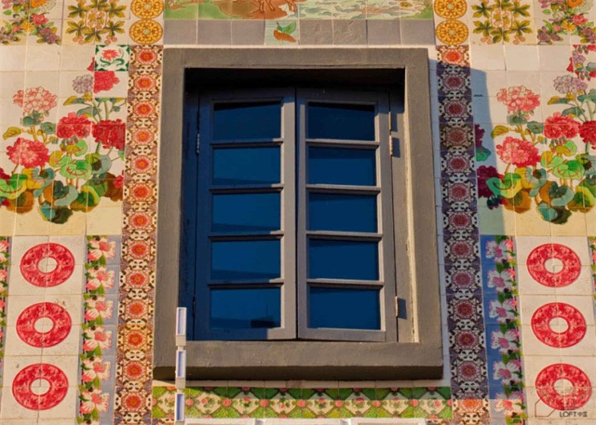 A closed window surrounded by colorful mosaic tiles with floral patterns and red circular motifs.