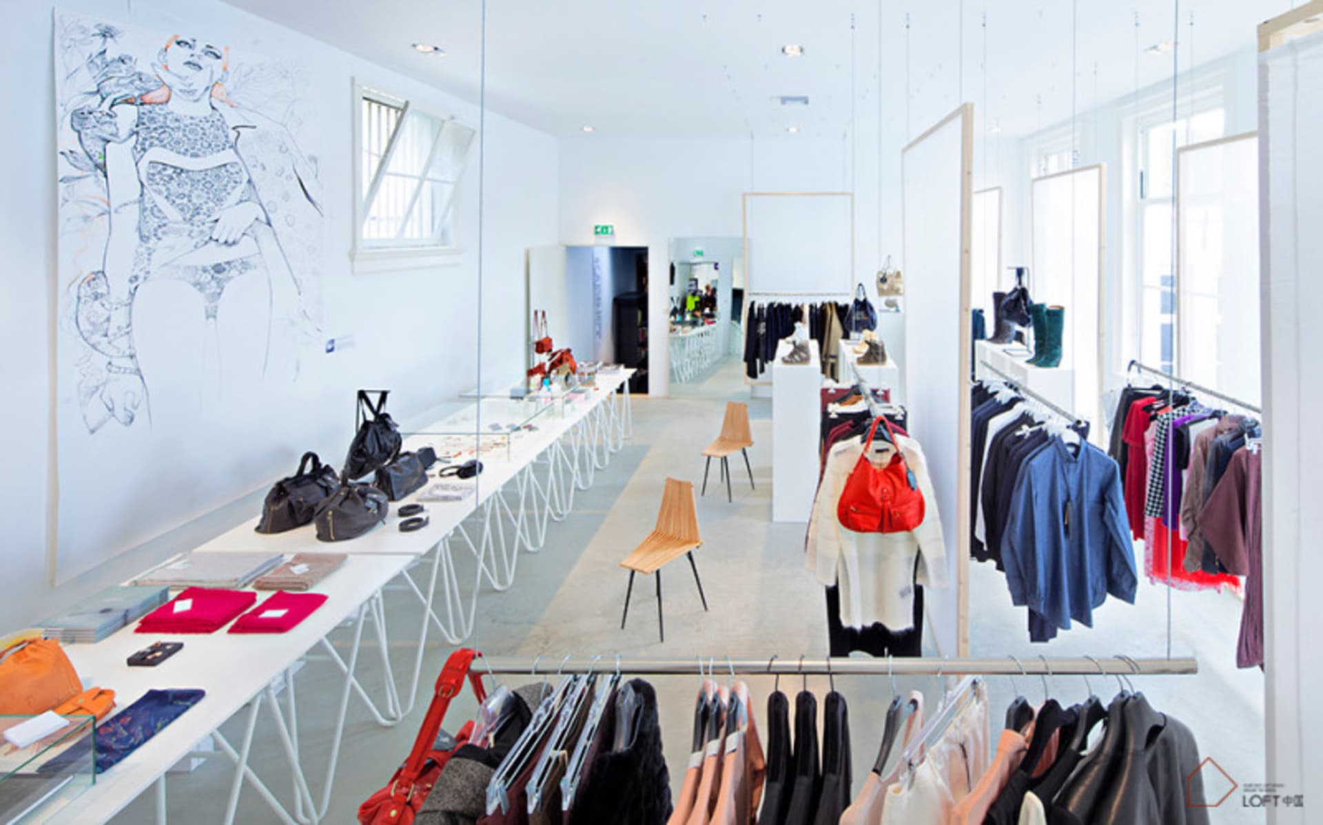 A modern clothing store with white walls, wooden chairs, and clothes displayed on racks.