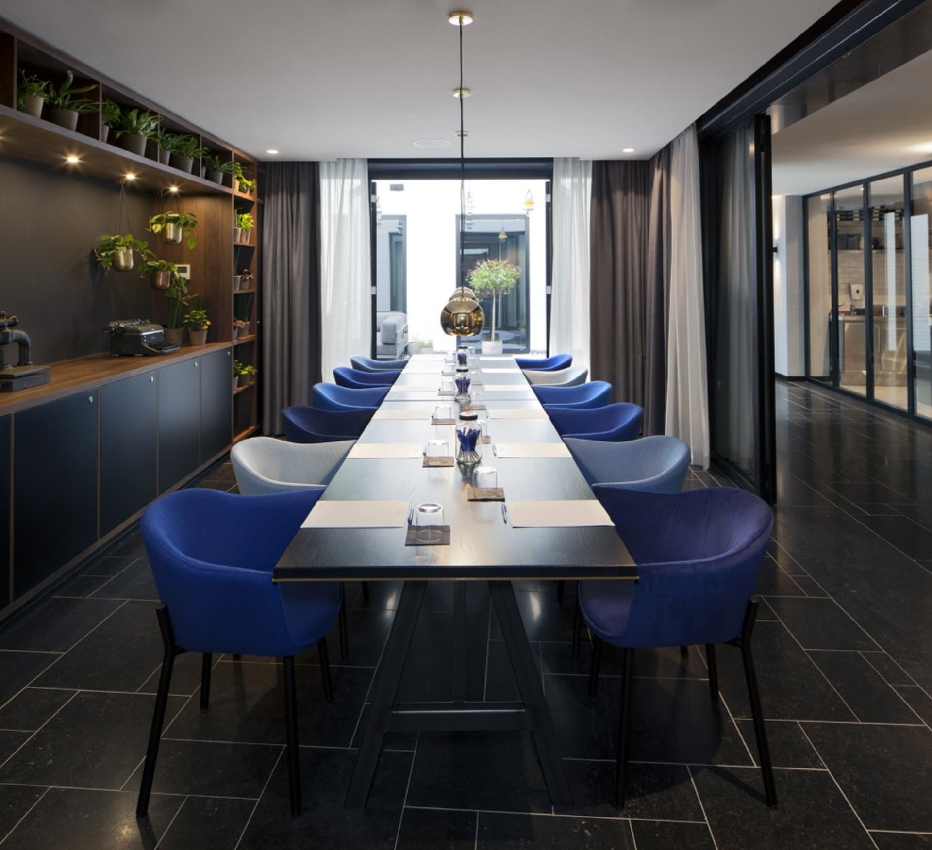 Modern conference room with long table, blue chairs, and green plants.