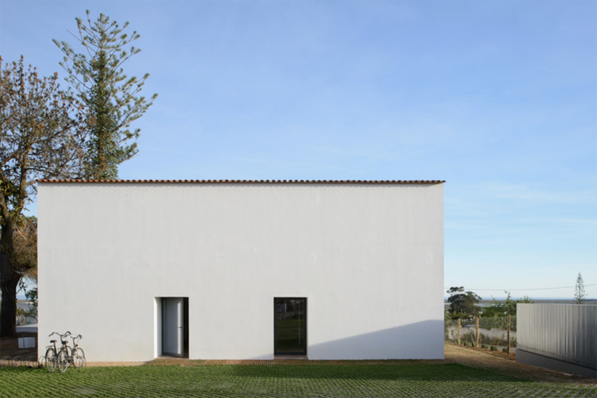 A minimalist modern white exterior building made of concrete with a single door and window.