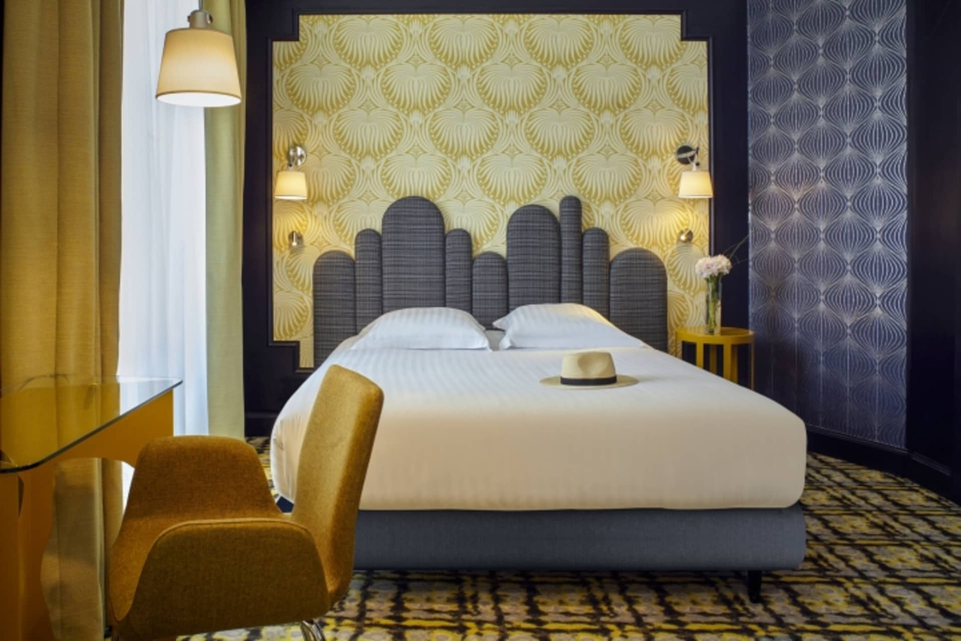 Modern hotel bedroom with white sheets, grey headboard, and mustard chair.