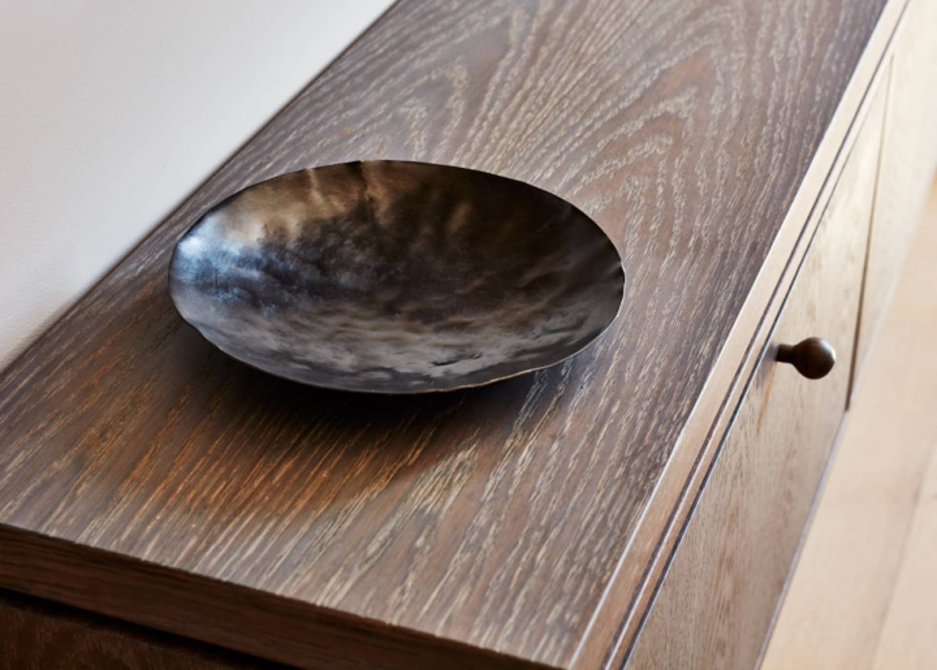 A sleek, minimalist wooden sideboard with a matte black serving bowl on top.